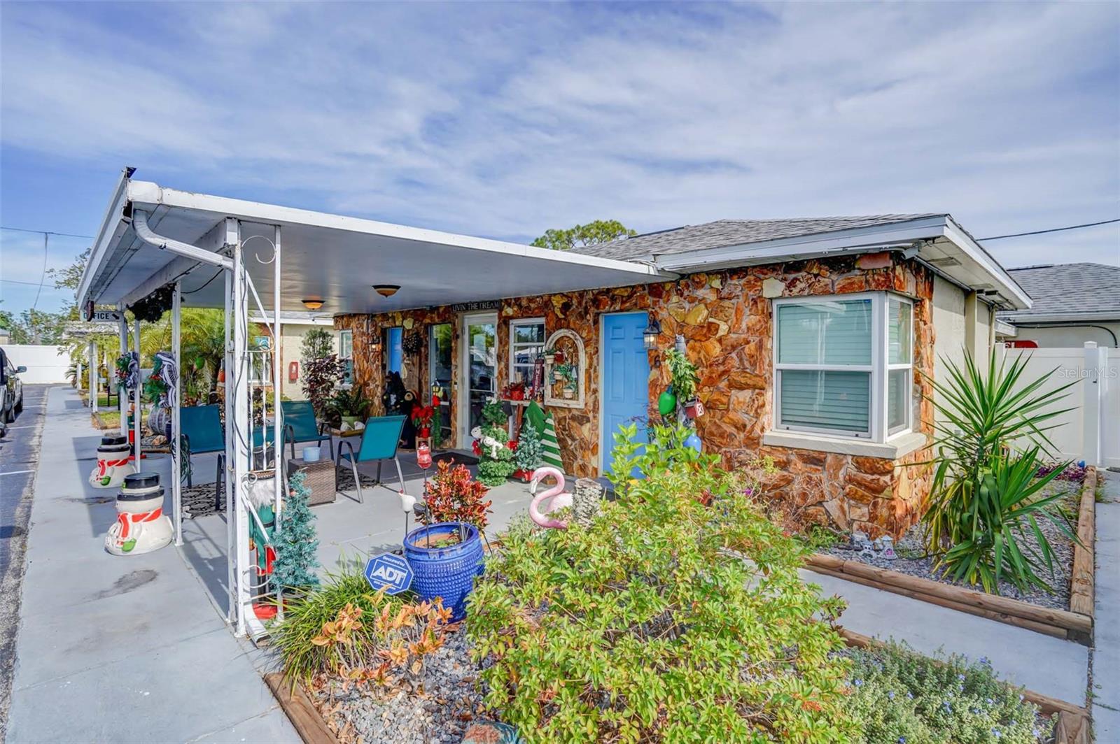 Stone-faced property with a covered porch, blue door, patio seating, and landscaped walkway.