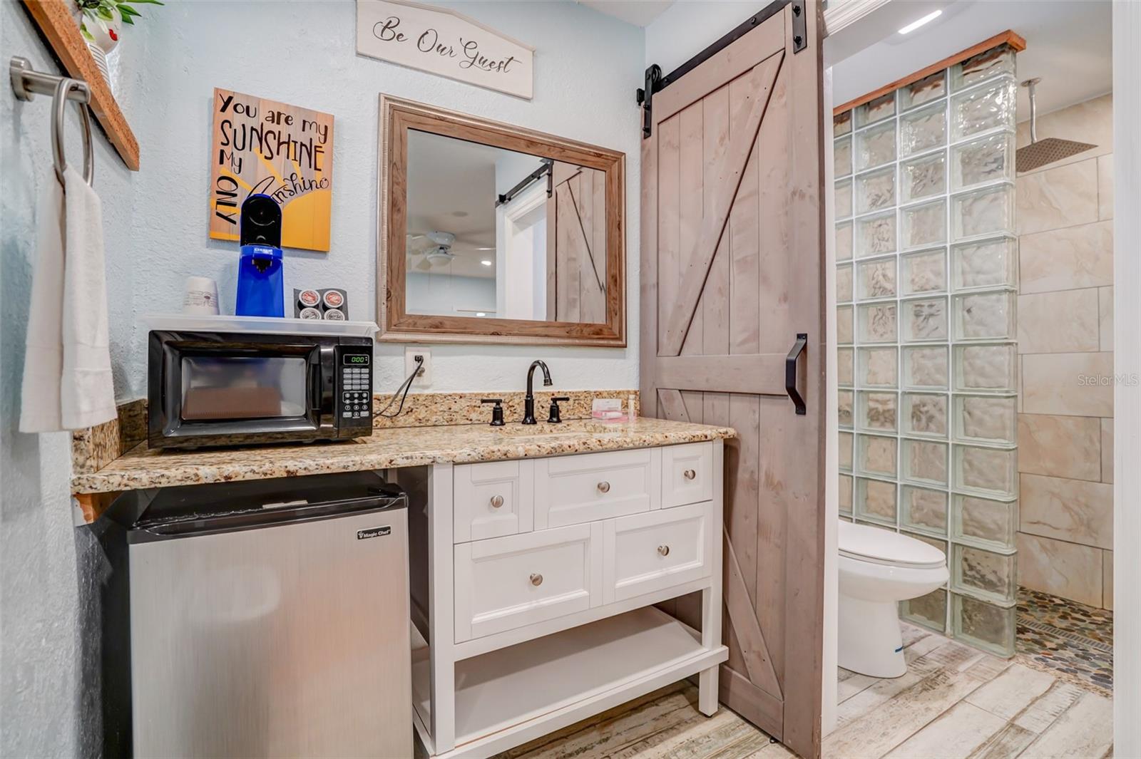 Bathroom vanity with granite counter beside a barn door opening to a glass-block shower.