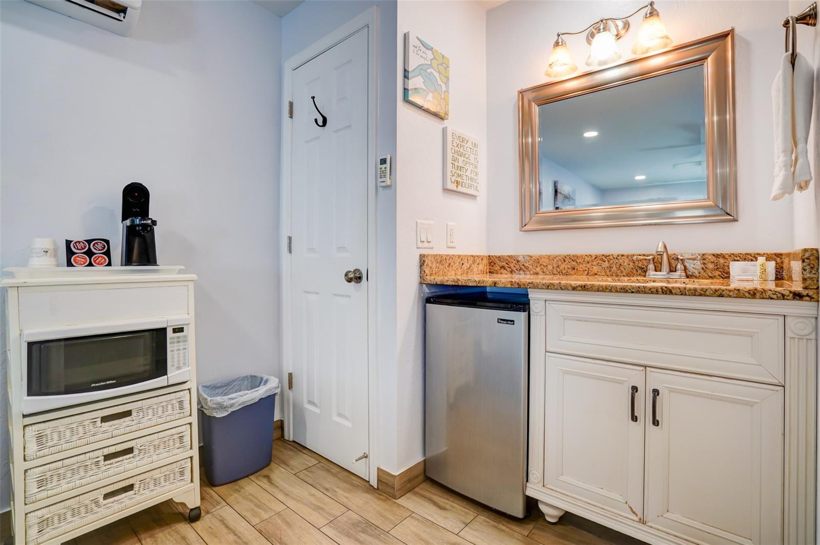 Bathroom vanity with granite counter and framed mirror, beside a compact refrigerator and microwave cart.