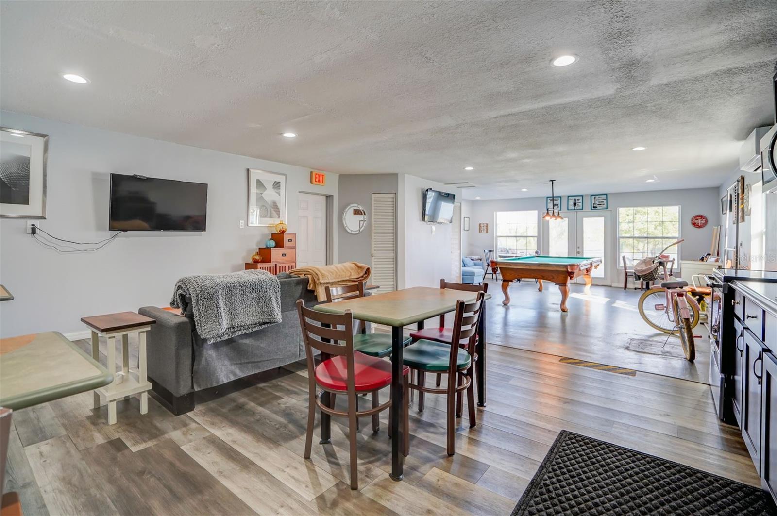 Recreation room with a pool table, sofa, and dining area by large windows.
