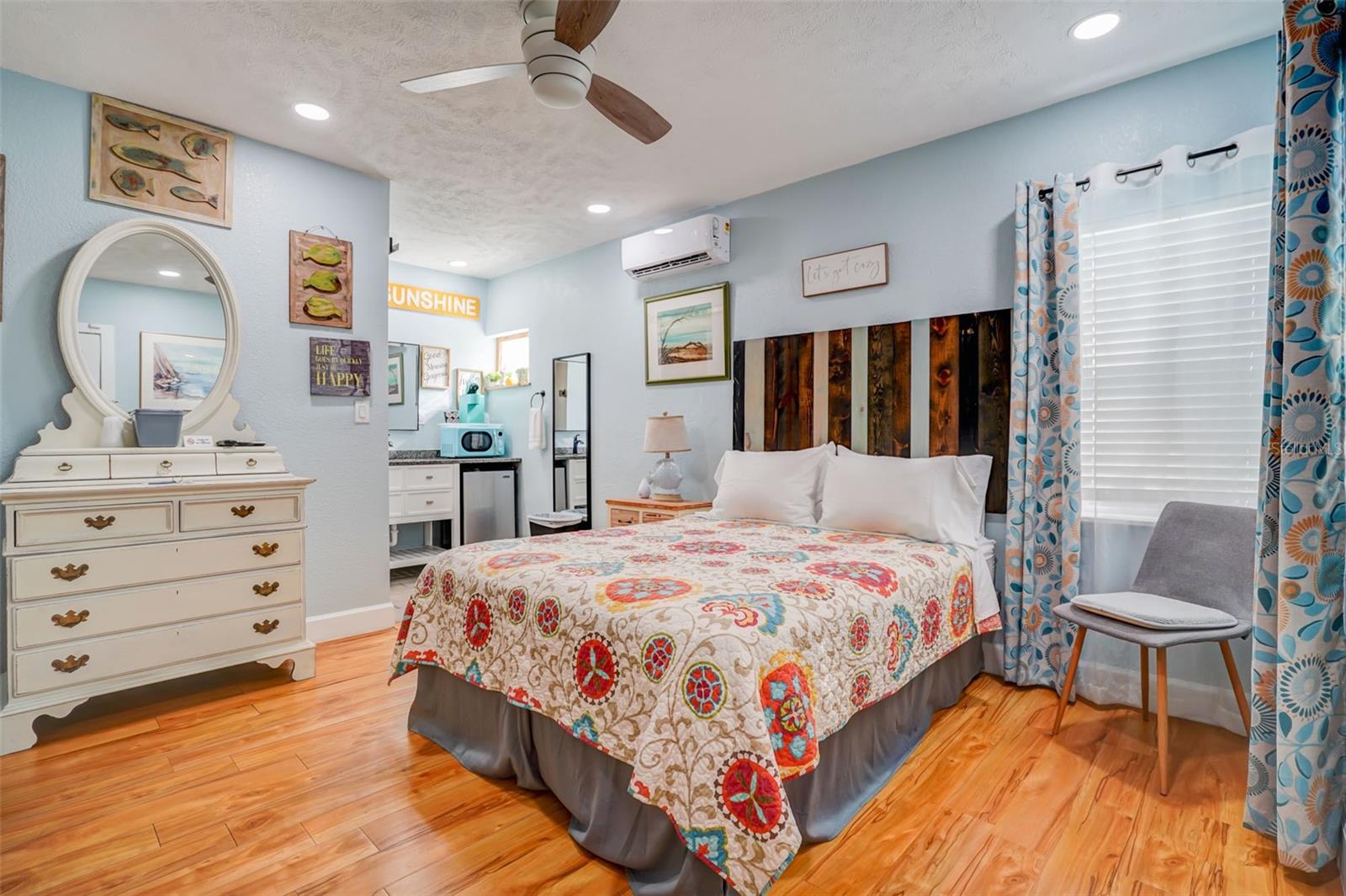 Bedroom with a colorful patterned bedspread, dark wood headboard, and white dresser with mirror.