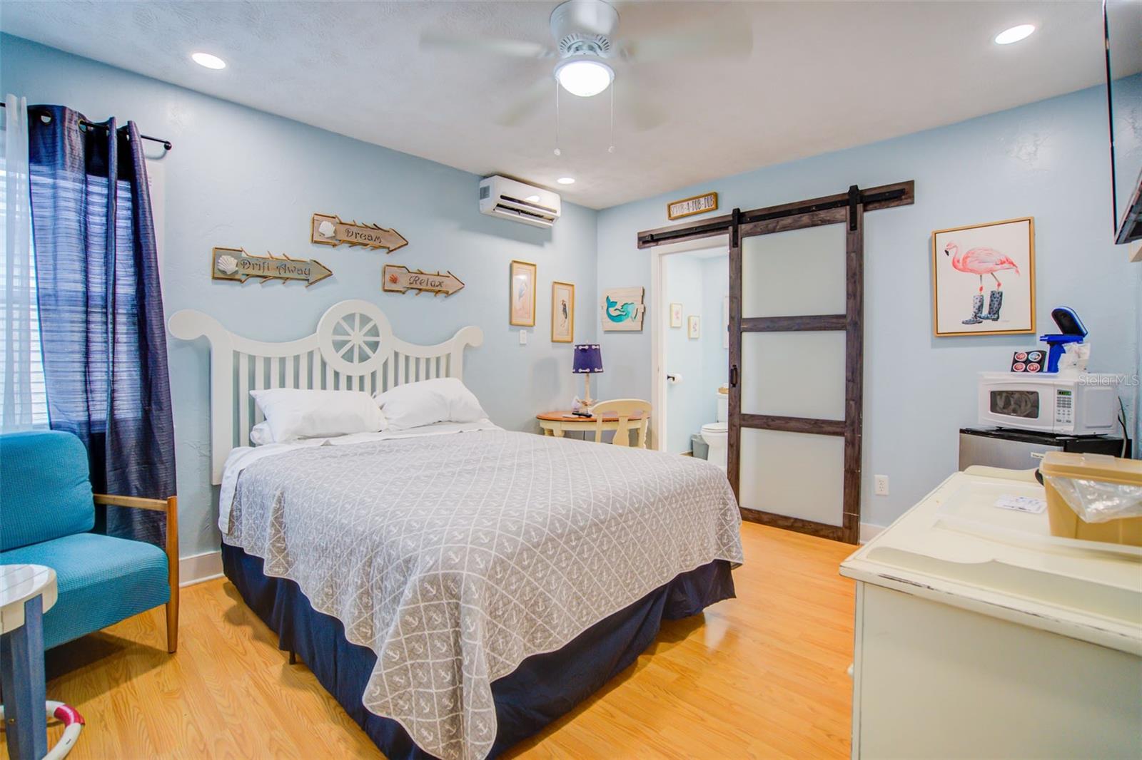 Furnished bedroom with a white bed, blue walls, and a dark wood sliding barn door.