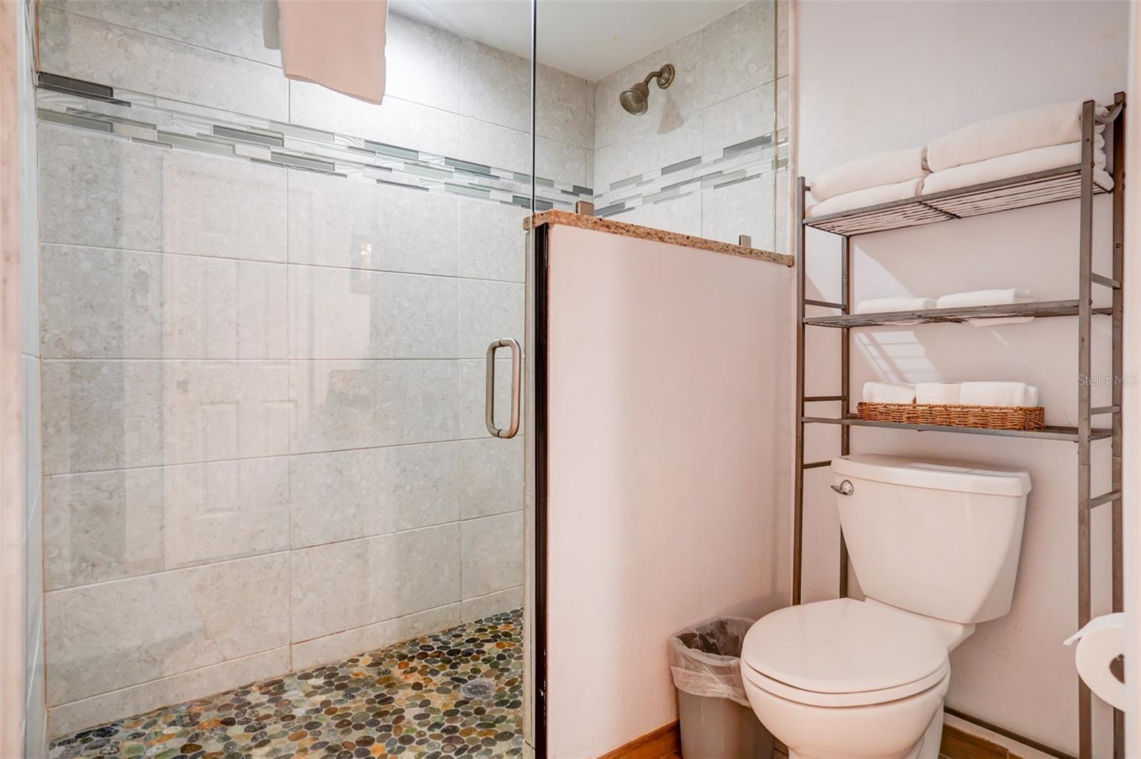 Bathroom with a pebble-floor walk-in shower and towel shelf beside the toilet.