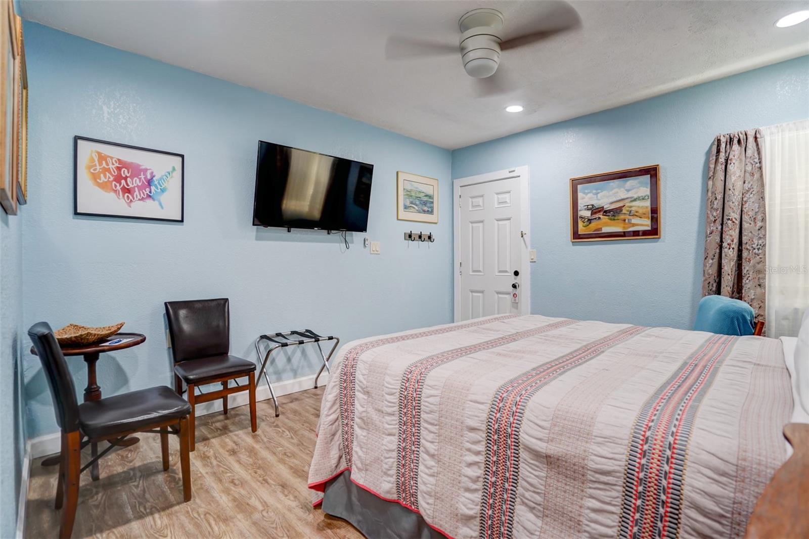 Bedroom with pale blue walls, a patterned quilt, and a wall-mounted television.