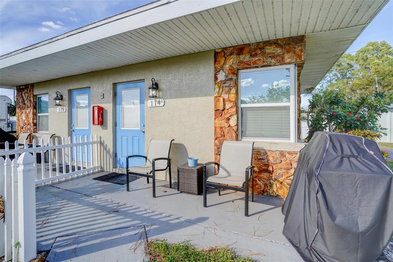 Property exterior with blue unit doors, stone accents, and a covered patio with chairs and grill.