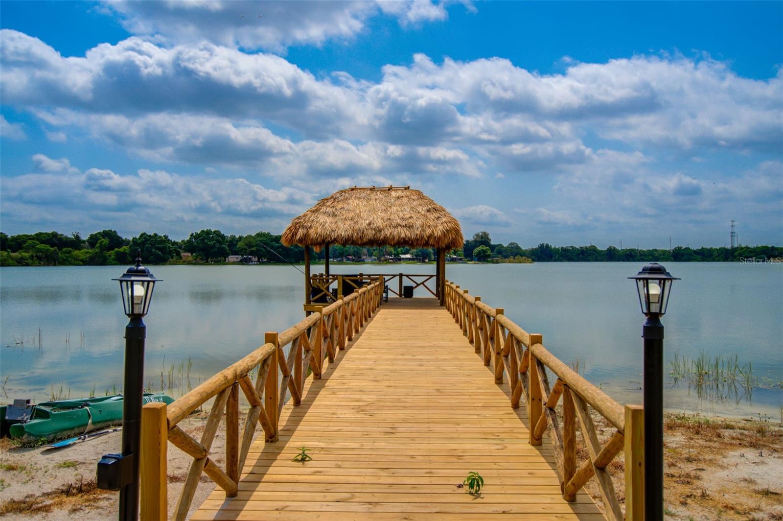 Wooden dock with thatched shelter extending into a lake, flanked by black lanterns.