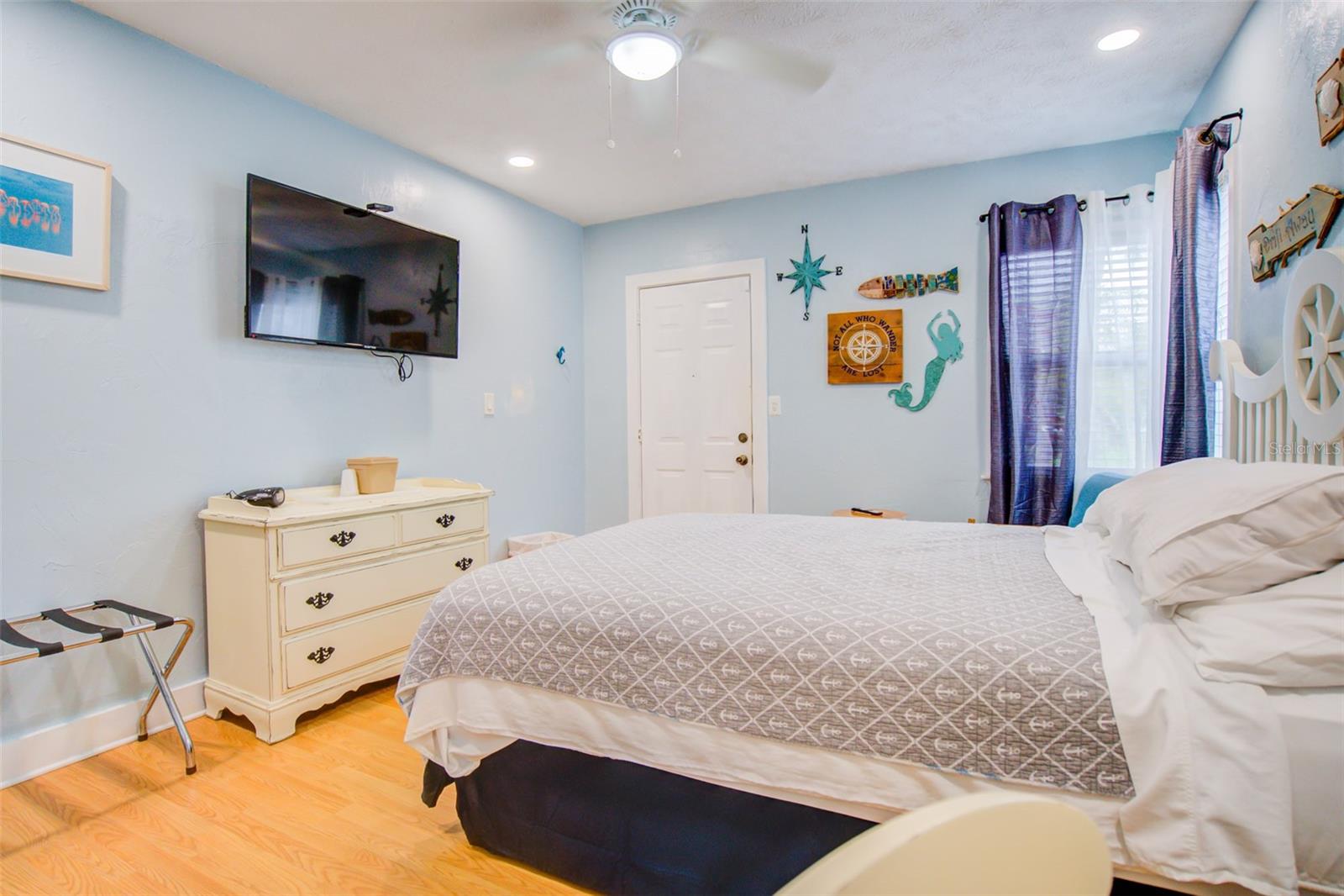 Bedroom with gray-patterned bed, white dresser, wall-mounted television, and nautical wall decor.