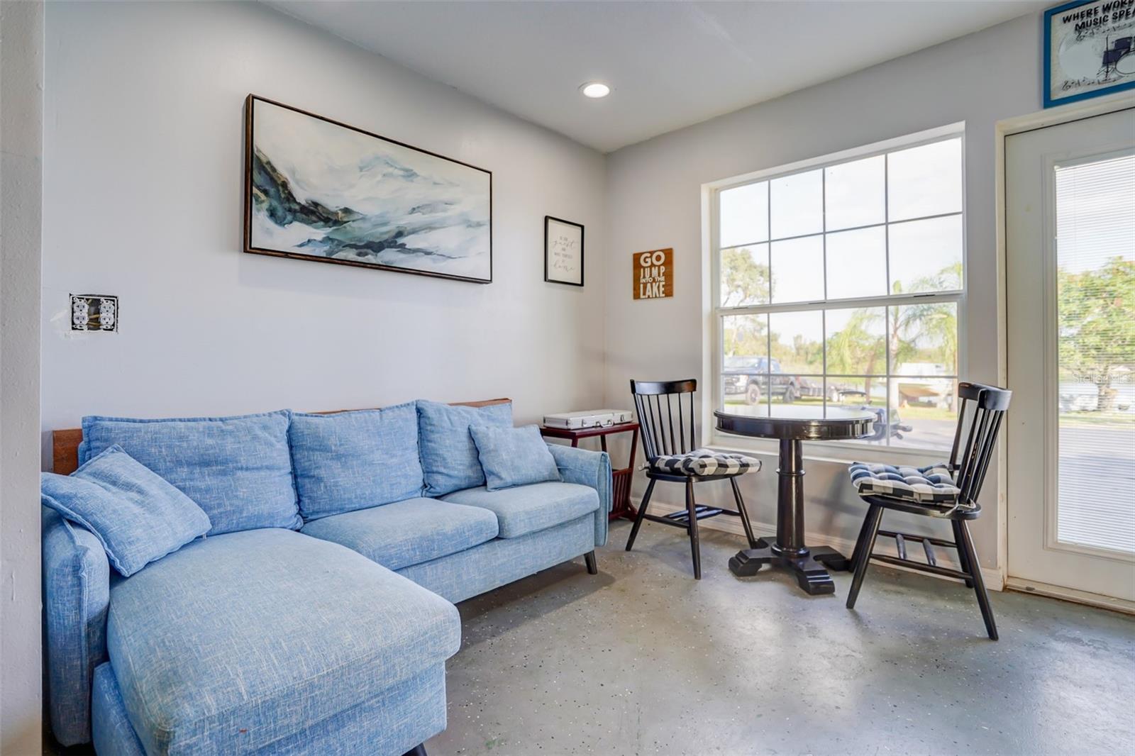 Living room with a blue sectional and a small dining table beside a large window.