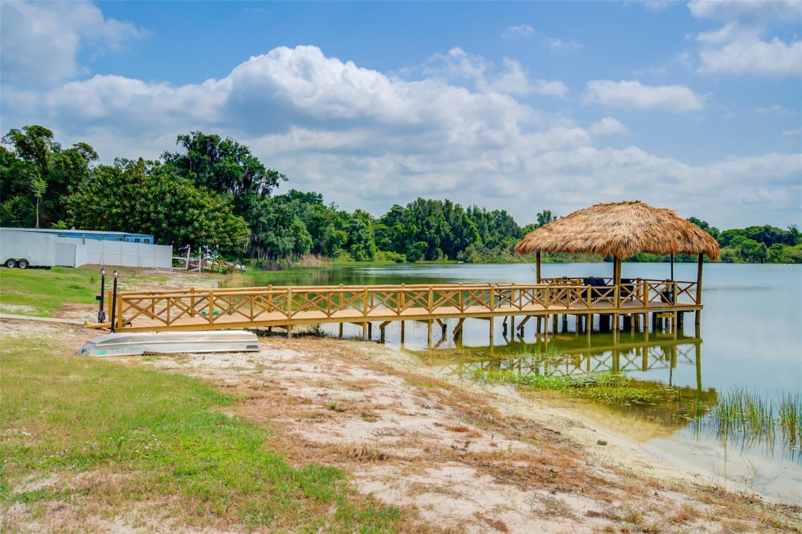 Wooden dock with a thatched-roof pavilion extending over a lake.