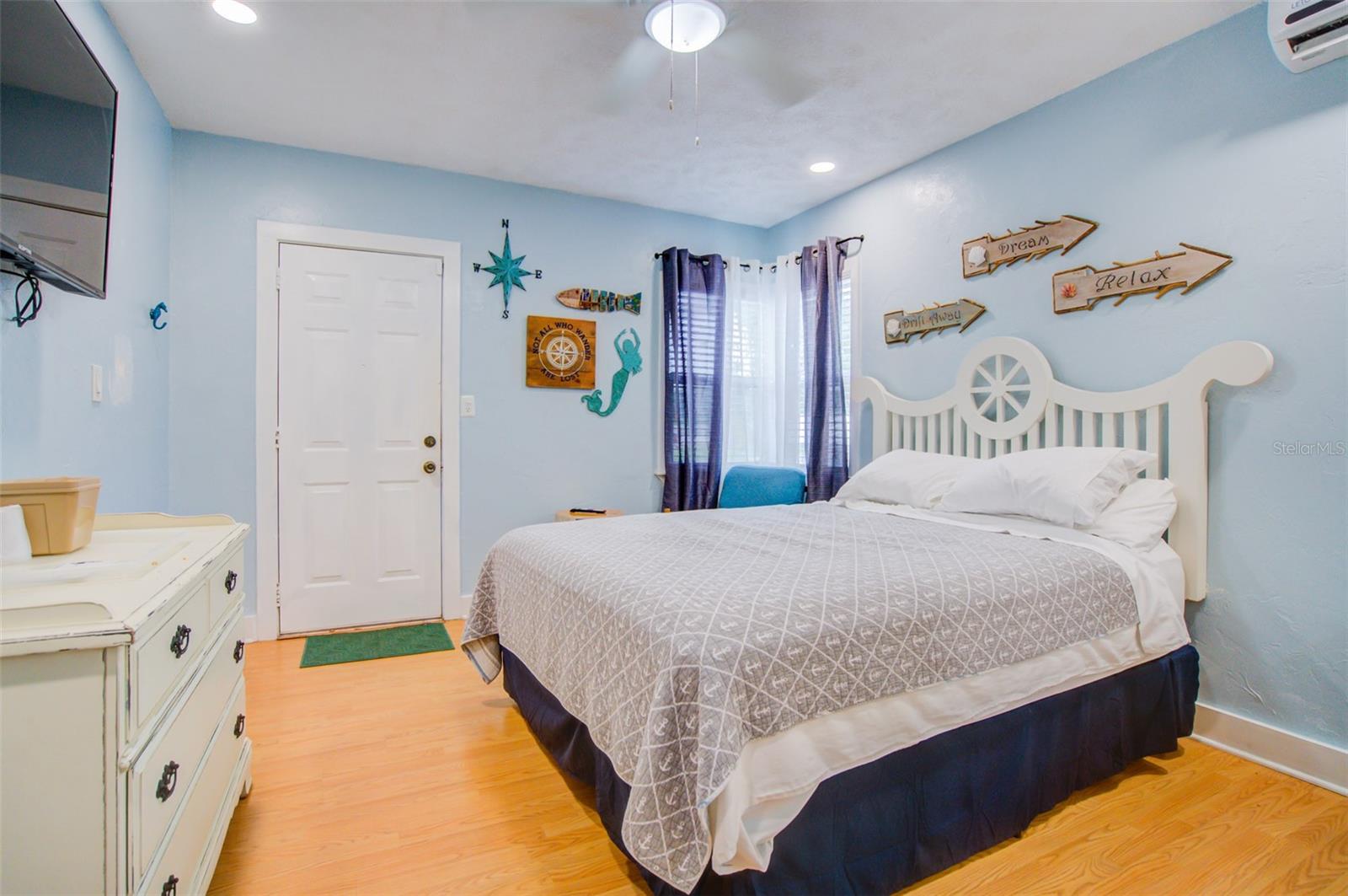 Bedroom with a white bed, pale blue walls, purple curtains, and coastal-themed decorations.