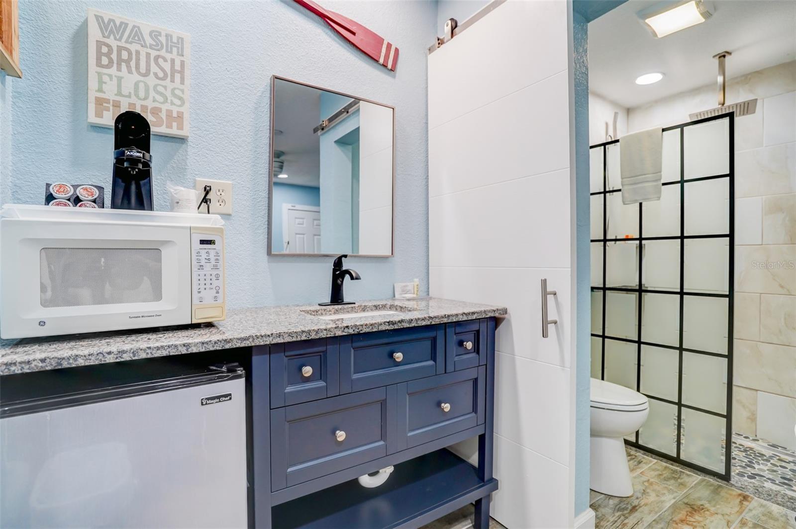 Bathroom with a blue vanity and granite counter beside a tiled shower with a black grid enclosure.