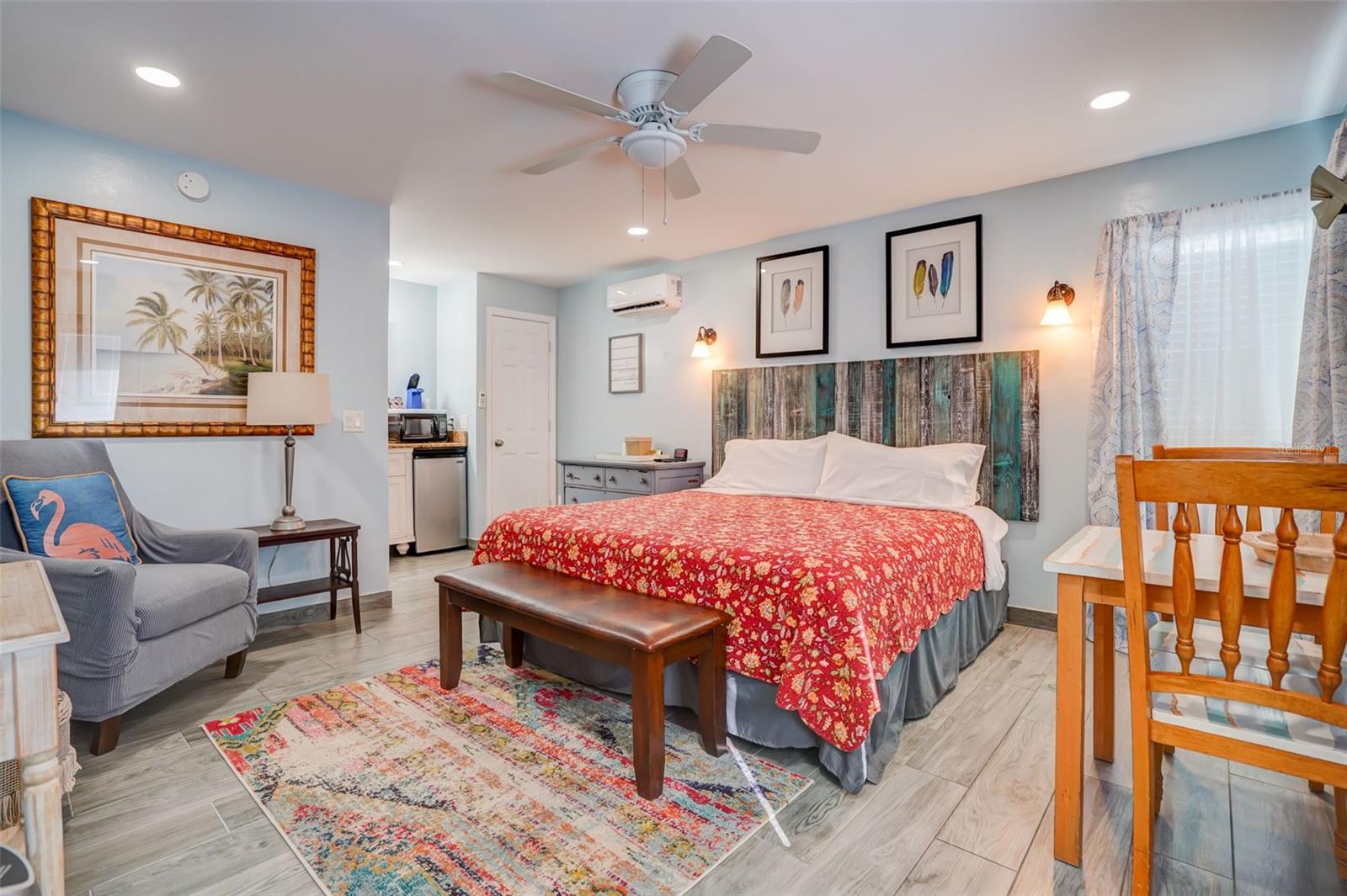 Furnished bedroom with a red floral bedspread, rustic wood headboard, and colorful rug.