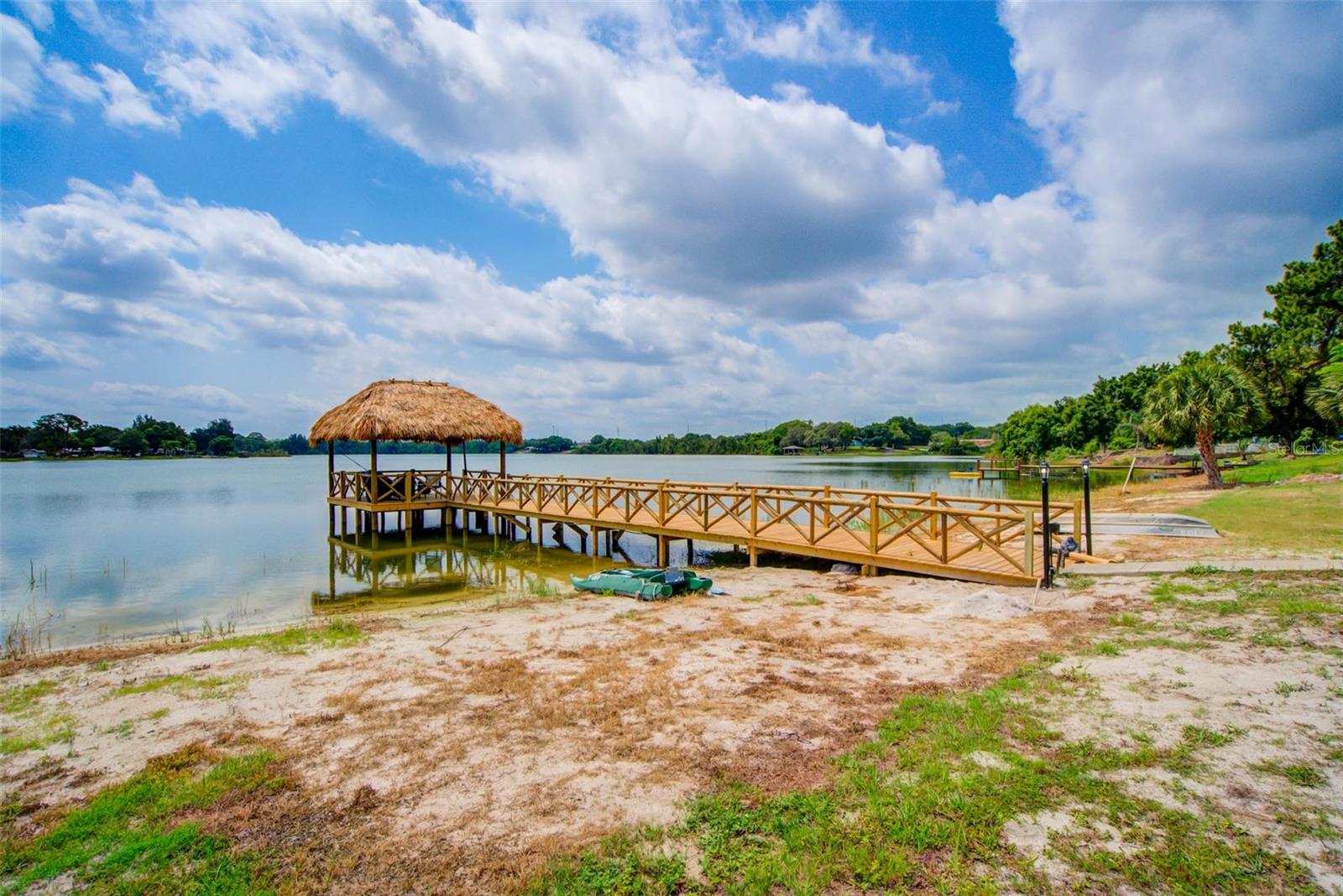 Wooden dock with a thatched-roof gazebo extending over a lake, with a small boat beside it.