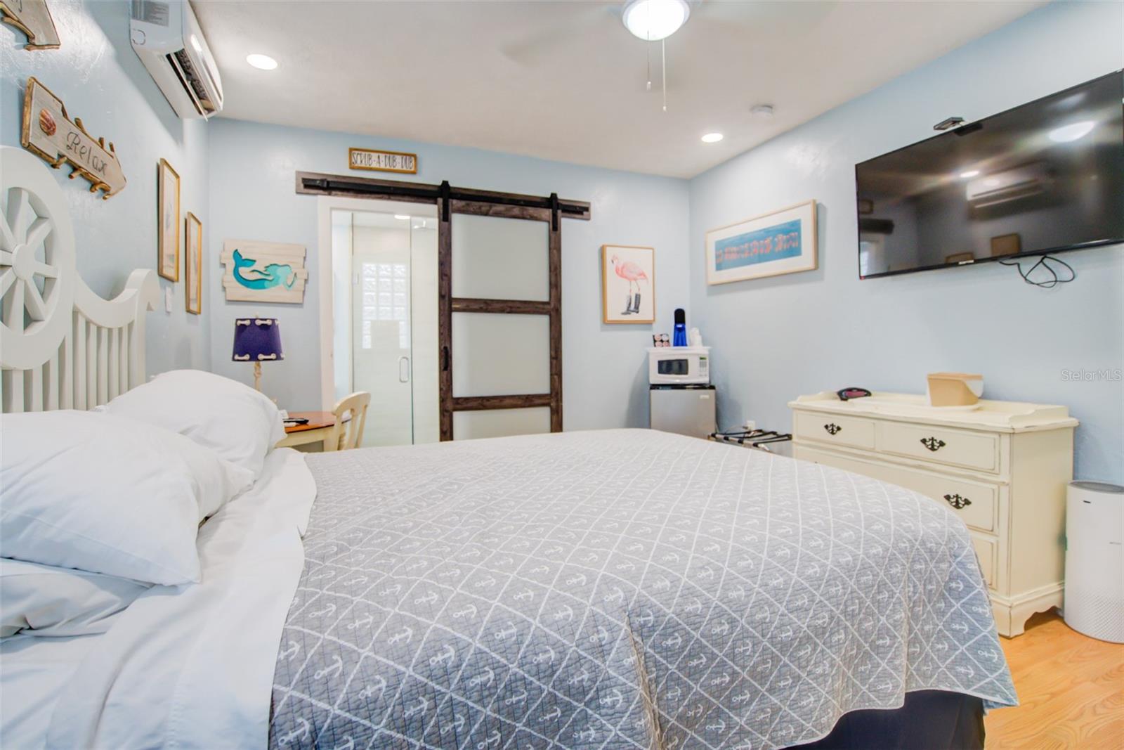 Bedroom with a gray patterned bedspread, white dresser, wall-mounted television, and dark wood sliding barn door.