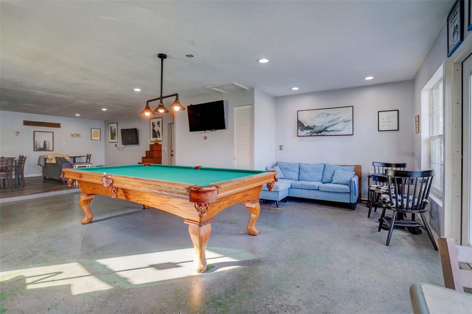 Recreation room with a large wooden pool table, blue sofa, and dining tables.