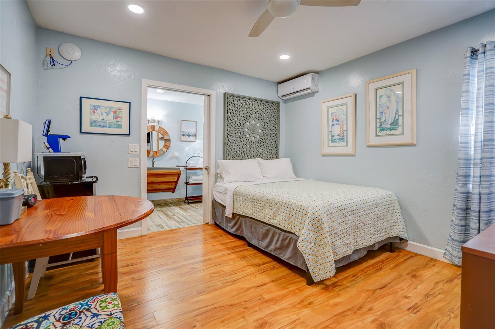 Bedroom with a patterned bedspread, warm wood flooring, and an adjoining bathroom.