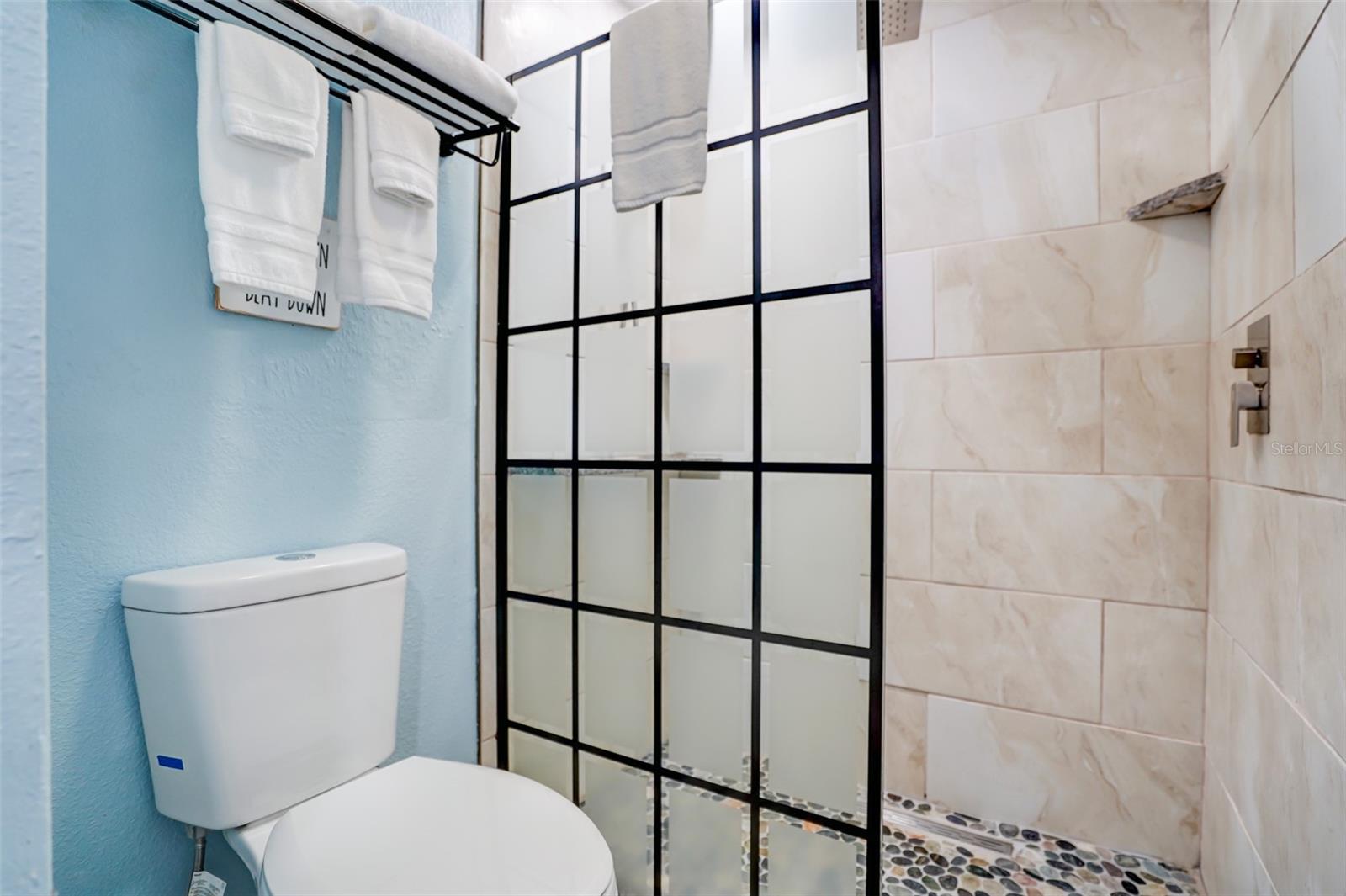 Bathroom with a black grid-pattern shower enclosure, marble-look tile, pebble floor, and white toilet.