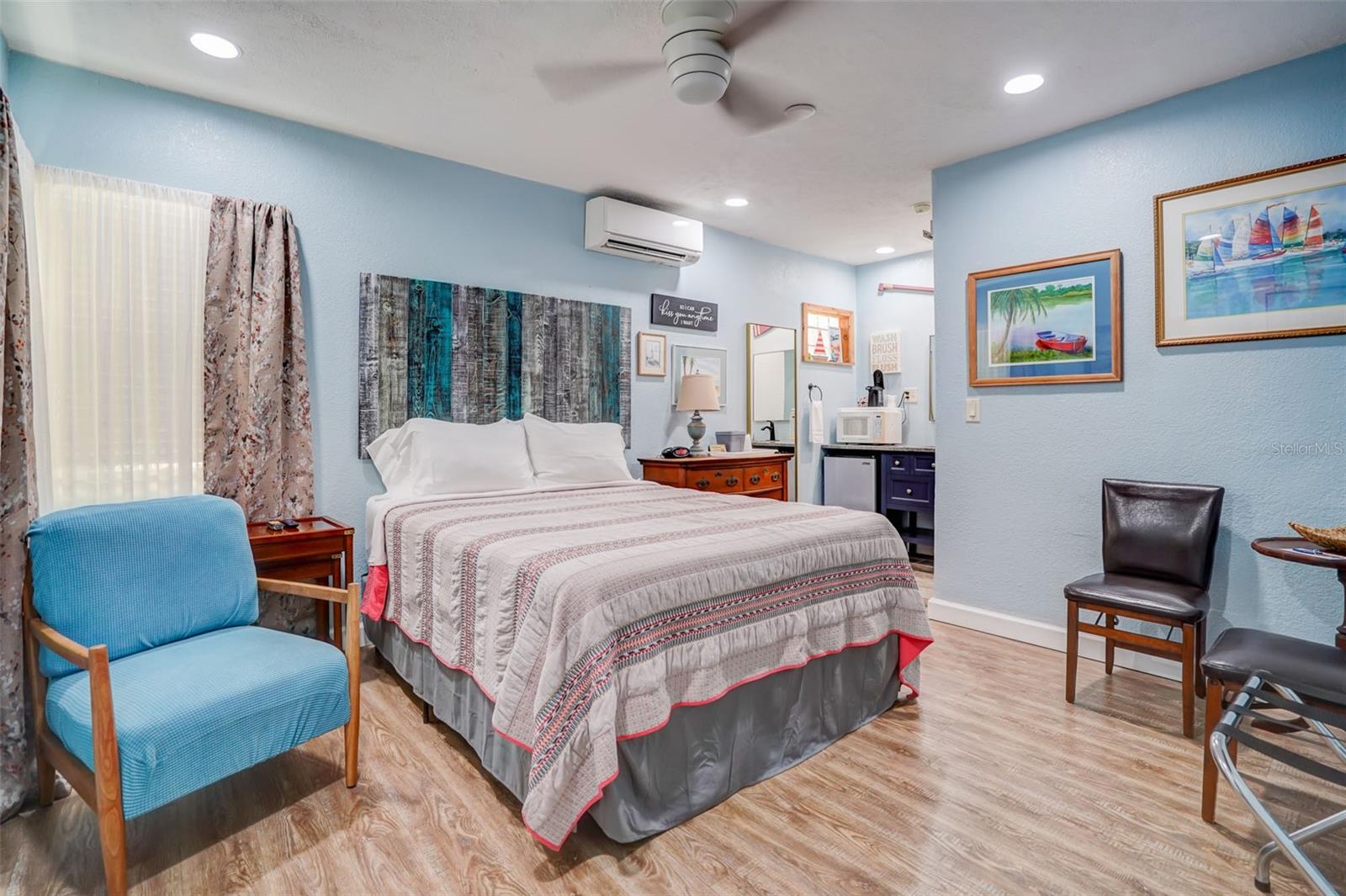 Furnished bedroom with a large bed, blue walls, and a compact kitchenette.