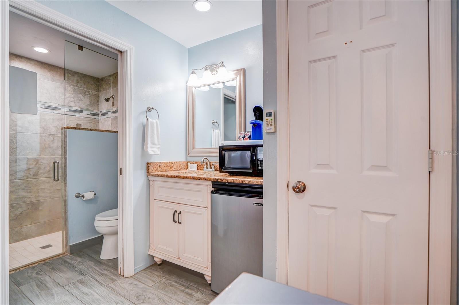 Bathroom with tiled glass shower, toilet, and vanity with granite counter and compact appliances.