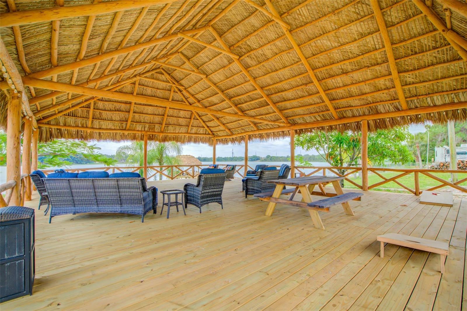 Covered thatched-roof pavilion with wicker seating and picnic tables overlooking the water.
