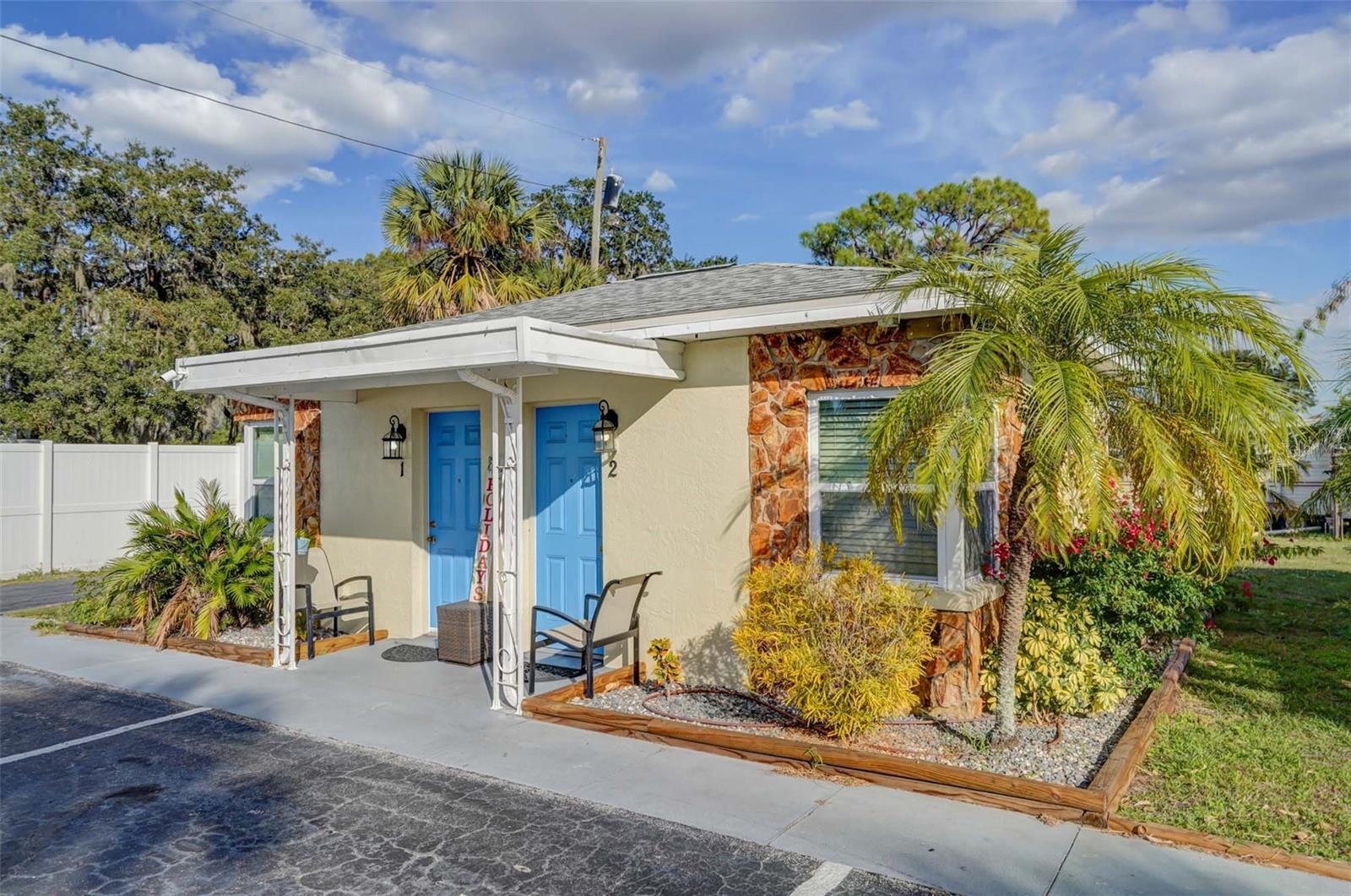 Small cream building with two blue doors, stone accents, and a palm-lined covered porch.
