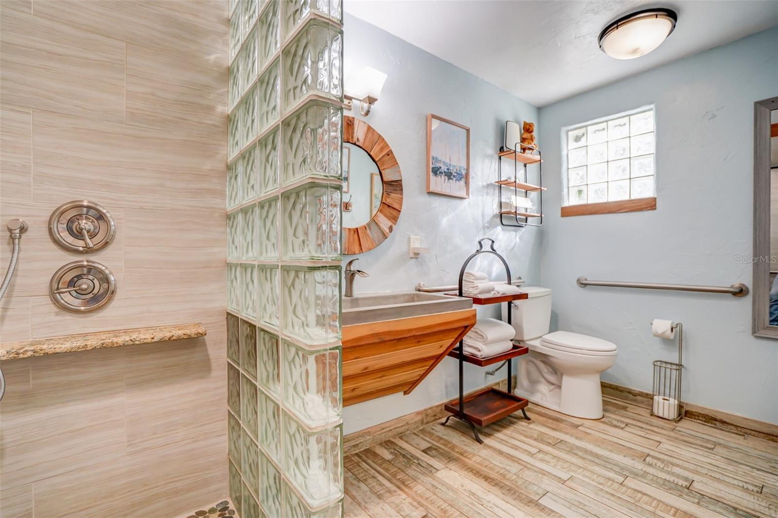Bathroom with a glass-block shower divider, wood vanity, and bright glass-block window.