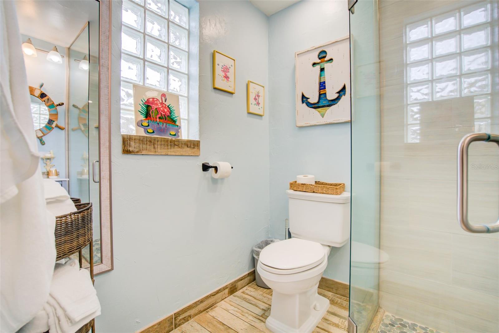 Bathroom with a glass-enclosed shower, glass-block windows, and colorful framed artwork.