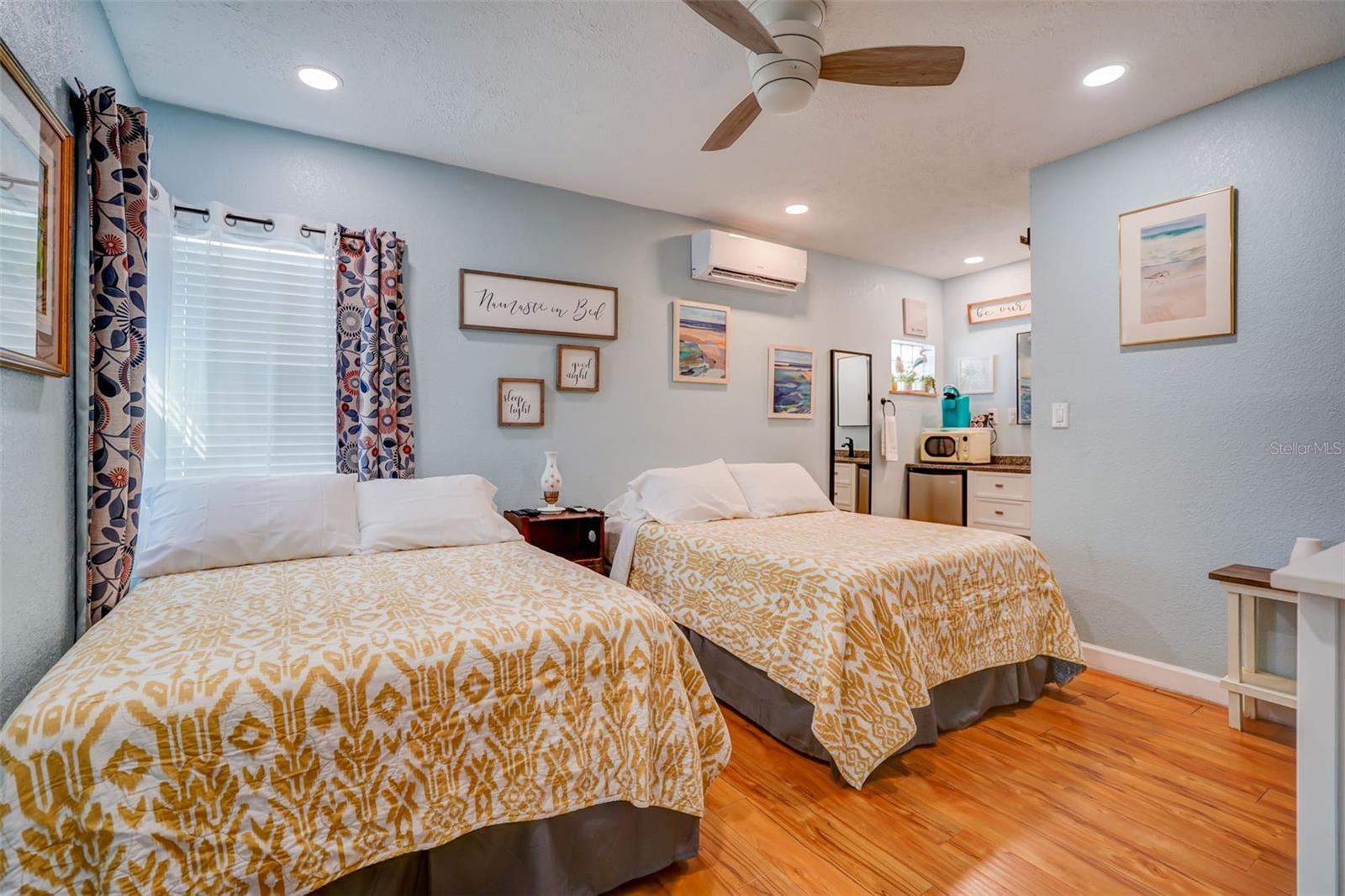 Bedroom with two patterned beds, pale blue walls, and wood-look flooring.