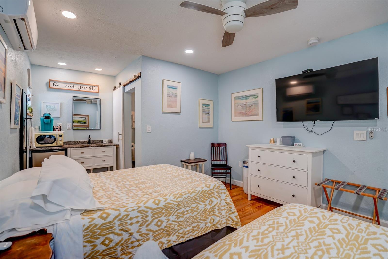 Furnished bedroom with two patterned beds, pale blue walls, and a wall-mounted television.