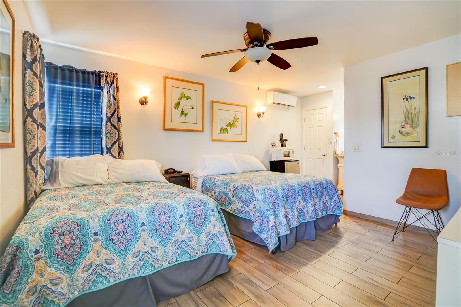Bedroom with two beds covered in colorful patterned quilts and a window with blue blinds.