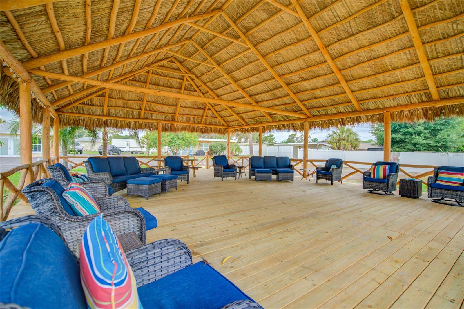 Covered patio with a thatched roof, wooden deck, and blue-cushioned wicker seating.