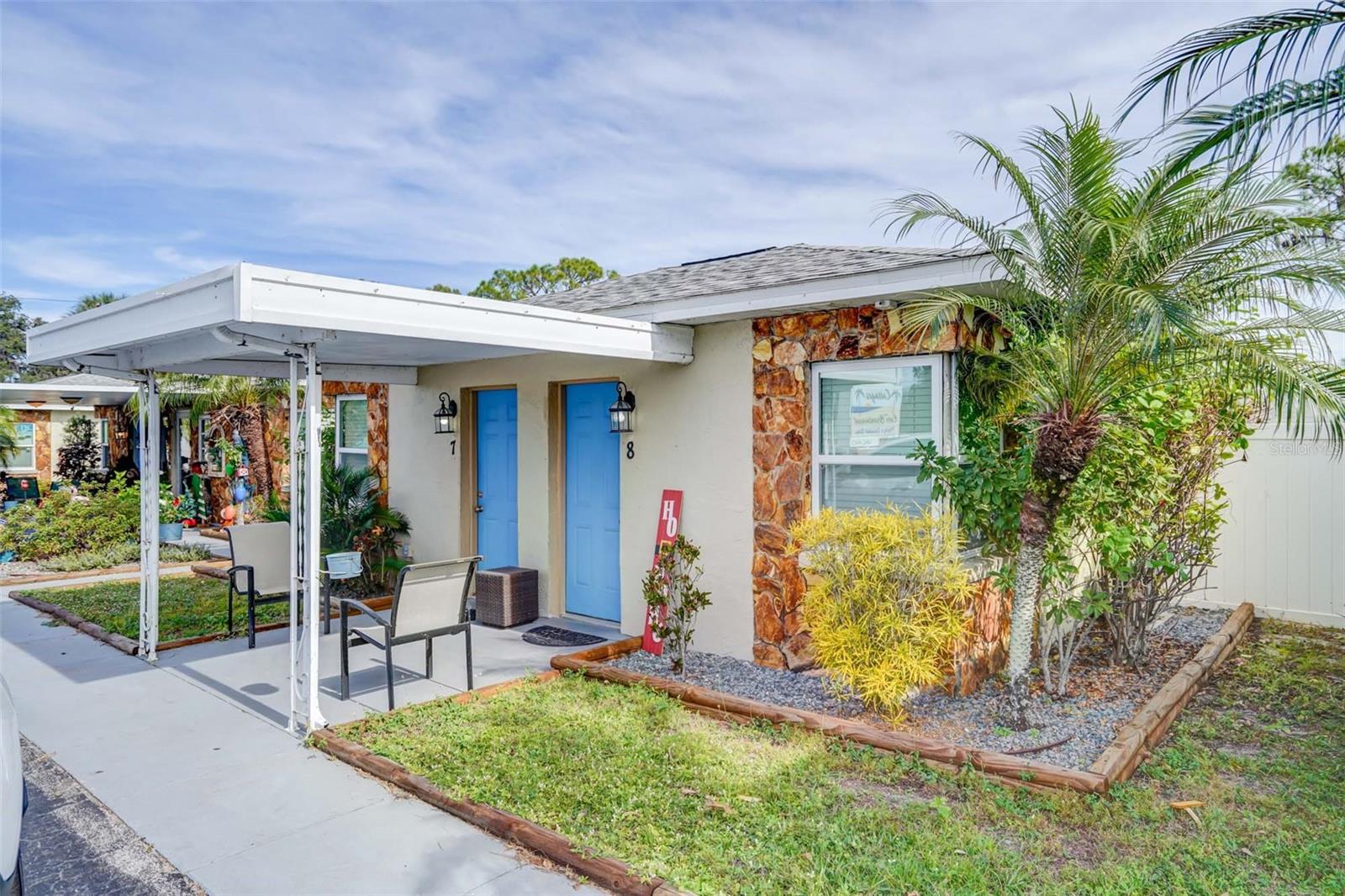 Residential building with two blue doors, a covered patio, stone accents, and palm landscaping.