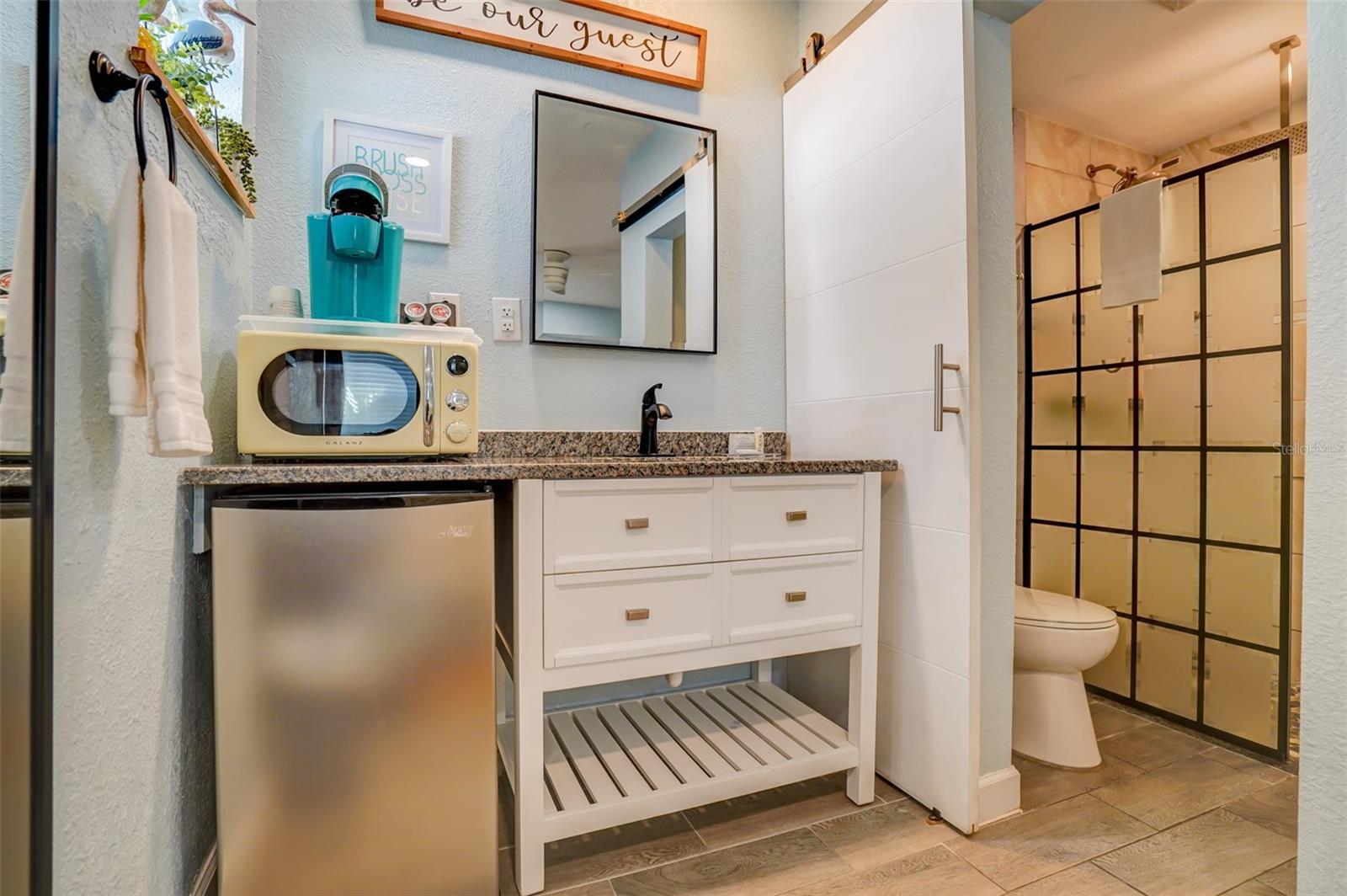Bathroom with a white vanity, compact mini fridge, and black-grid glass shower enclosure.