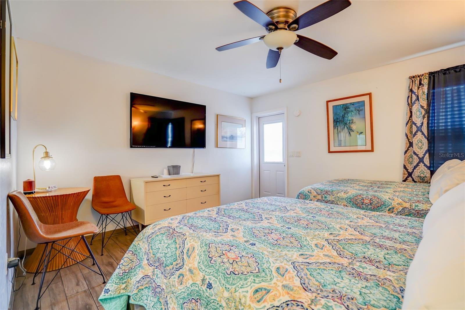 Furnished bedroom with patterned beds, a ceiling fan, and a wall-mounted television.