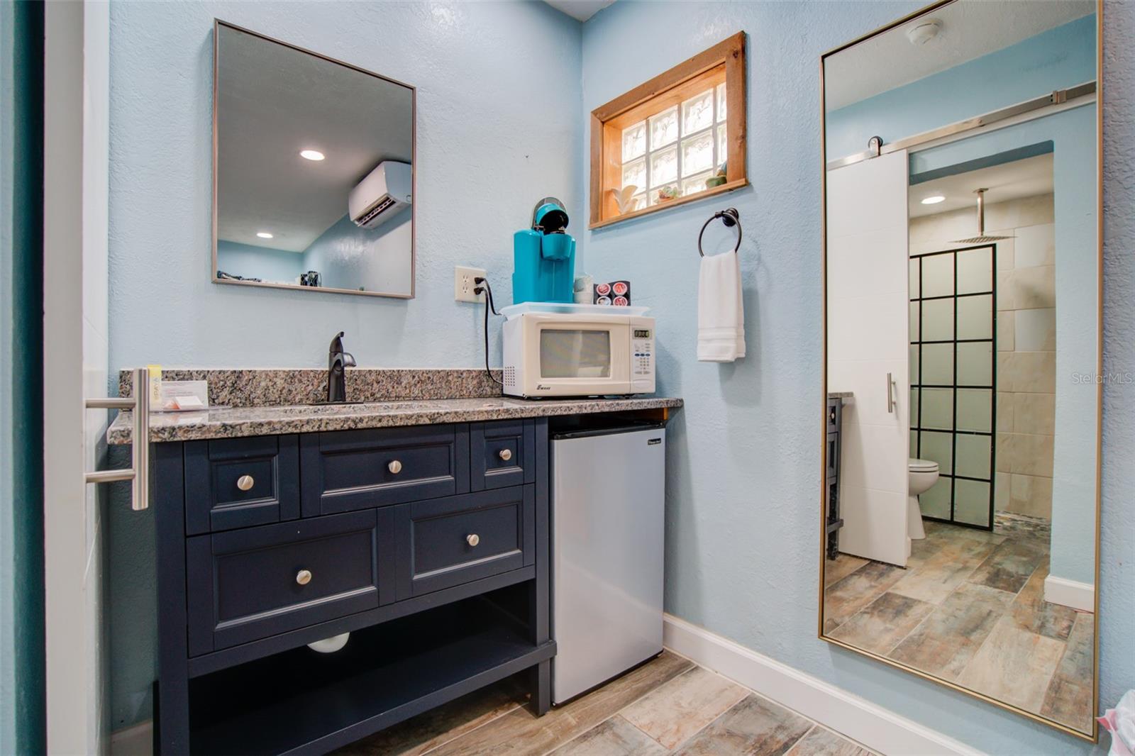 Bathroom with a navy vanity, countertop microwave, compact refrigerator, and reflected walk-in shower.