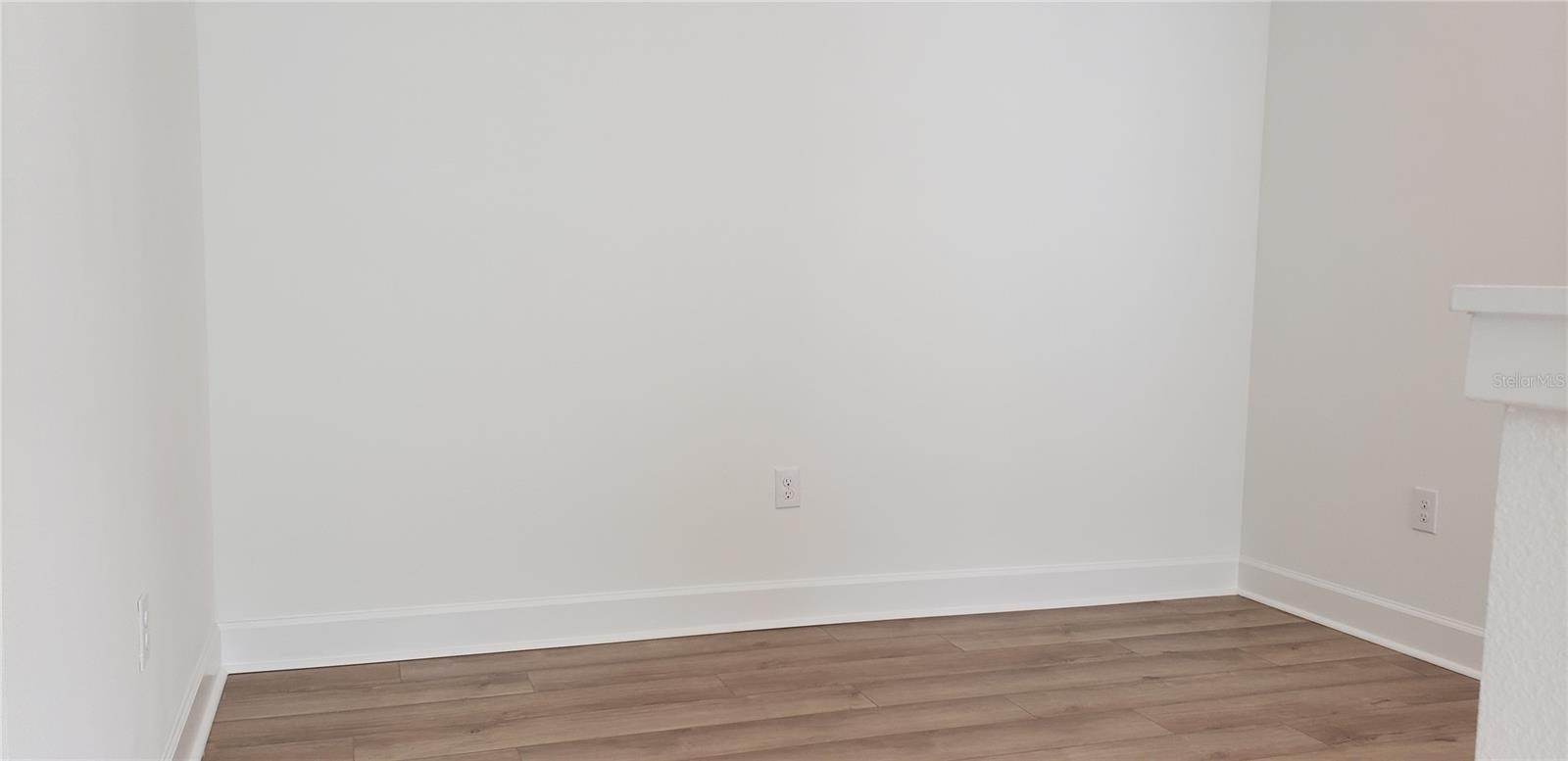 Empty room with wood-look plank flooring and part of a fireplace.