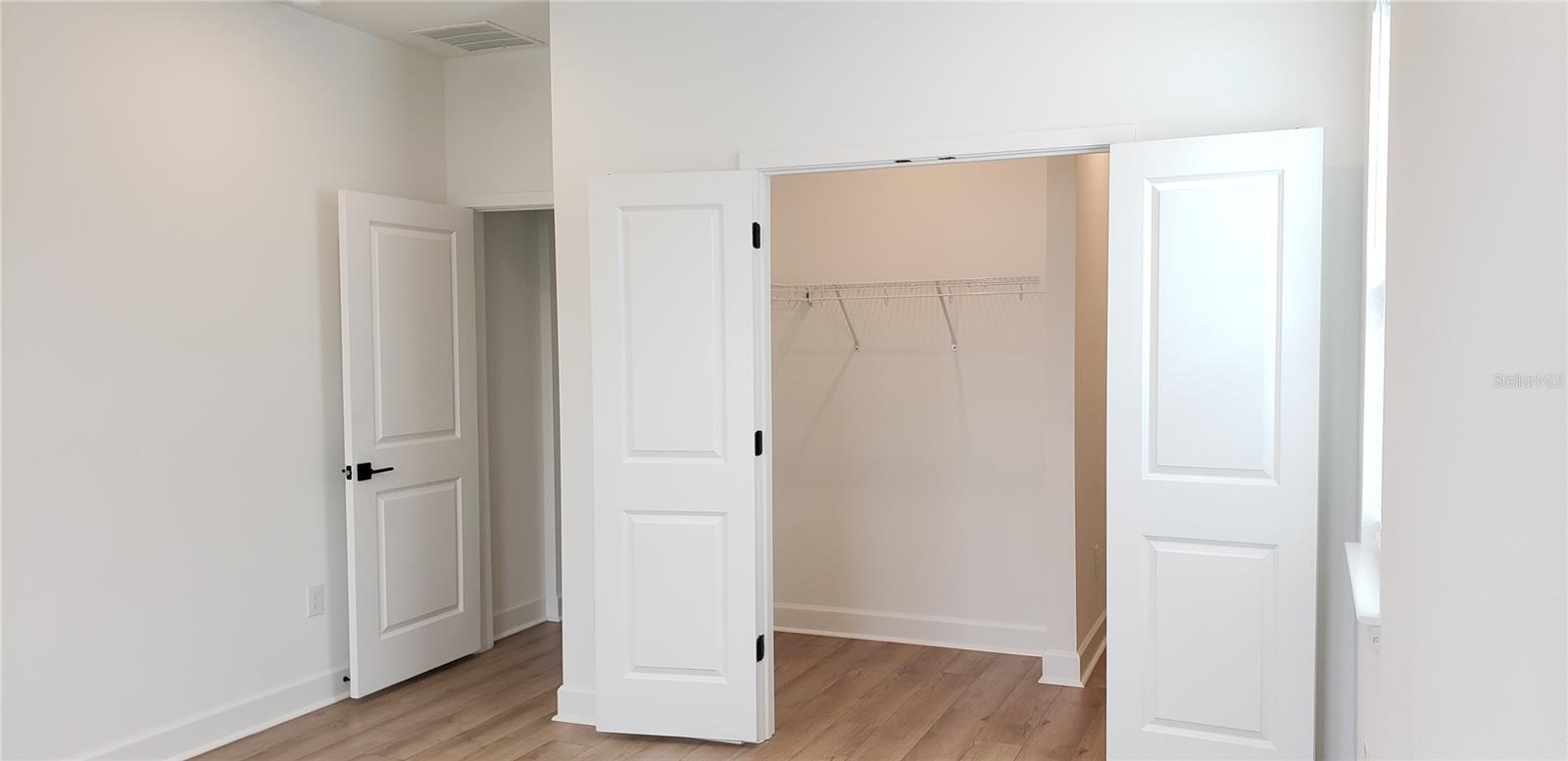 Open bedroom closet with wire shelving, white doors, and wood-look flooring.