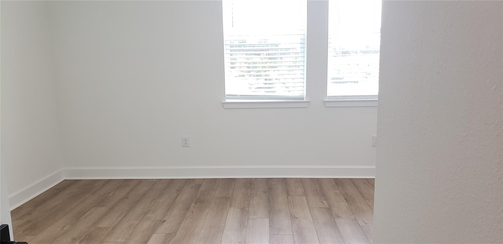 Empty room with wood-look flooring, white walls, and two windows with blinds.