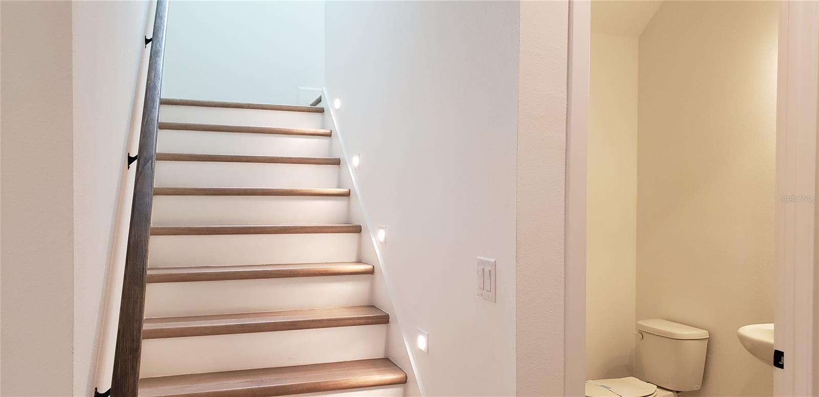 Interior staircase with wood treads, illuminated step lights, and an adjacent bathroom.