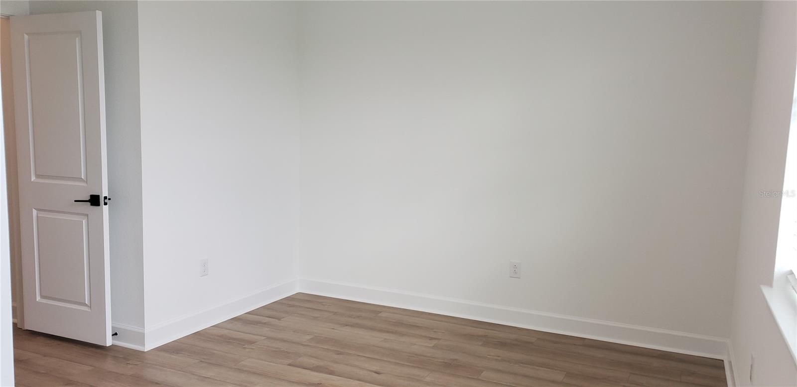 Empty room with white walls, wood-look plank flooring, and an open door.
