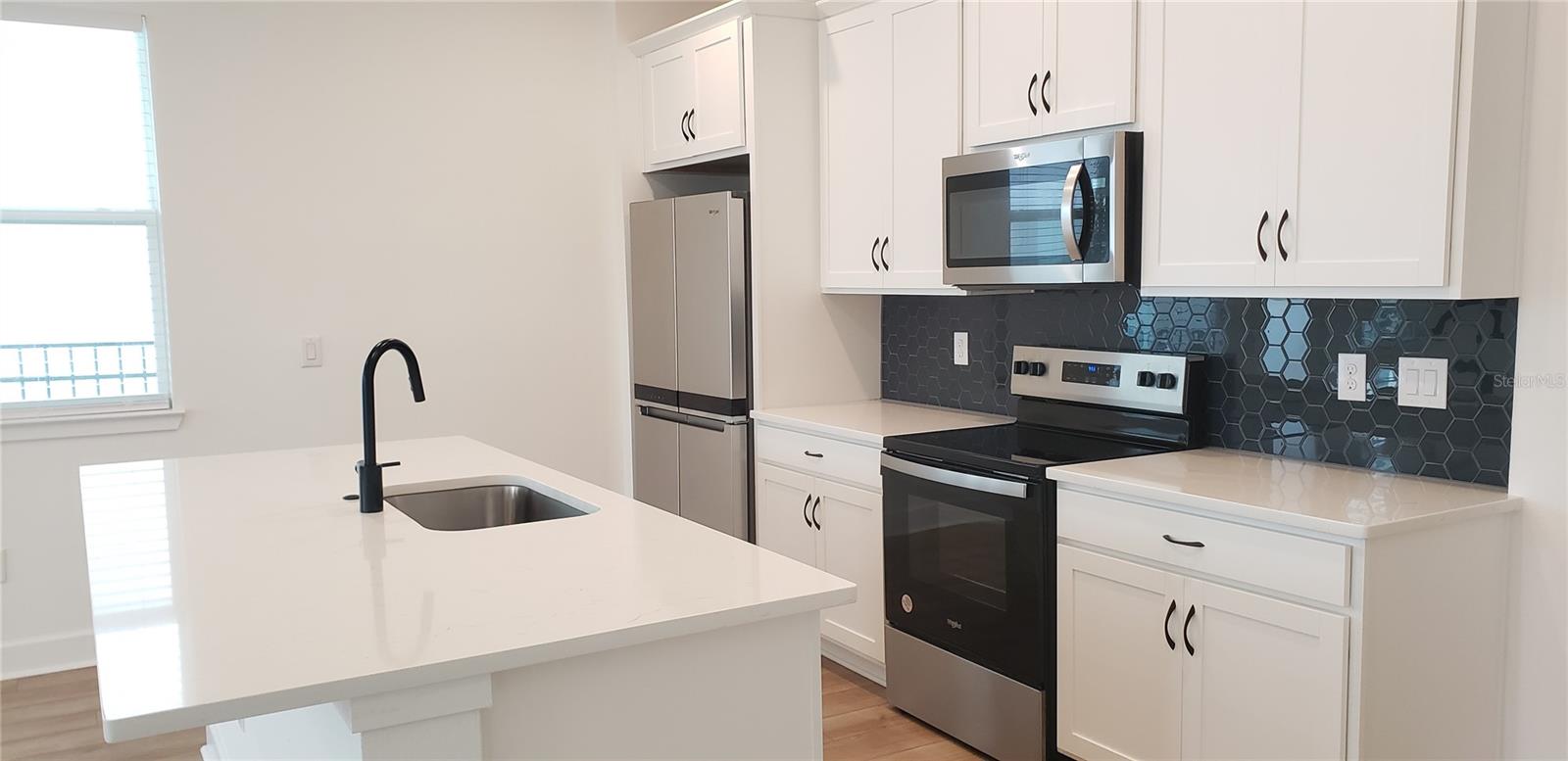 Kitchen with white cabinets, a large island, stainless steel appliances, and a dark hexagonal backsplash.
