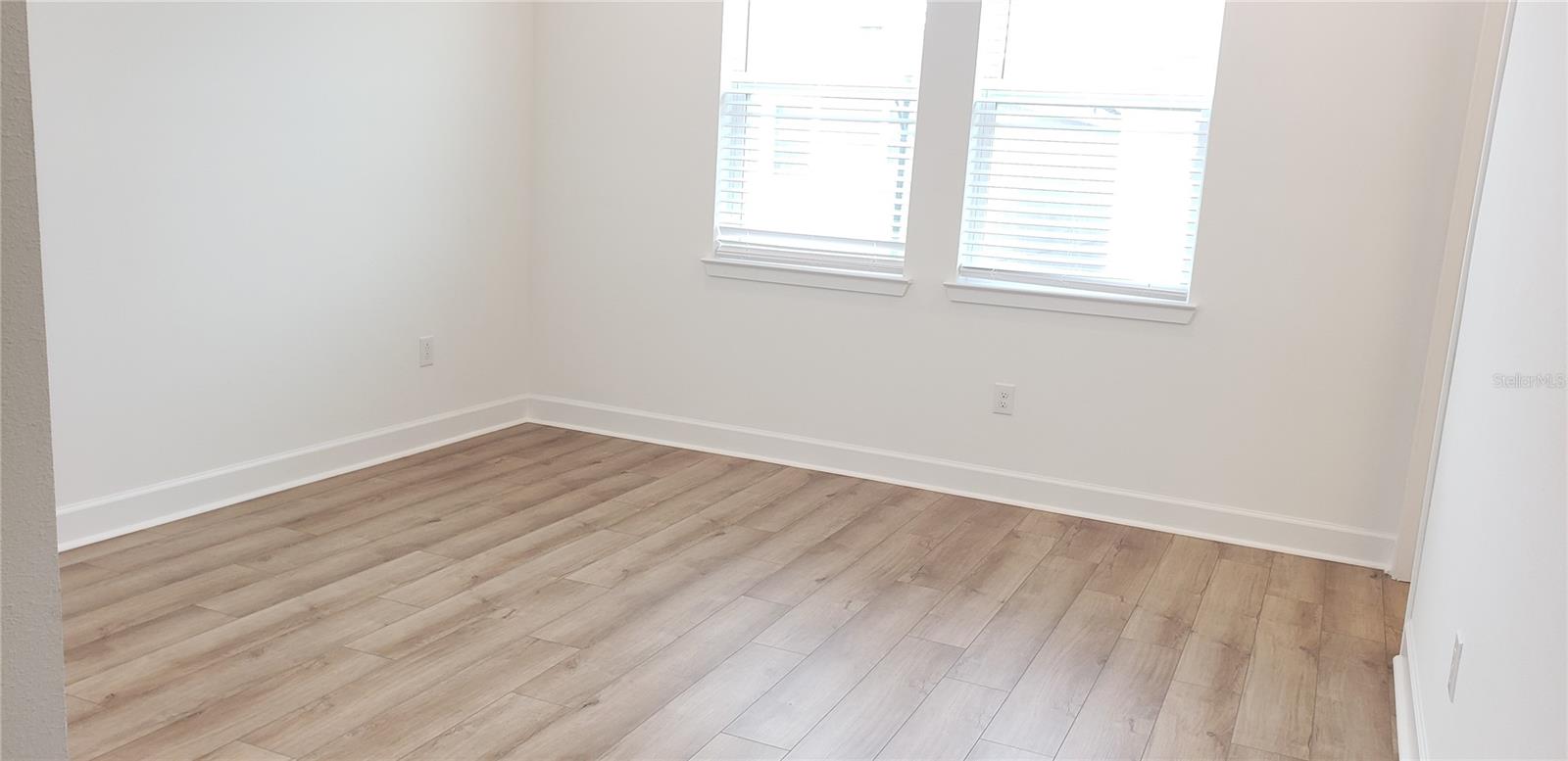 Empty room with wood-look plank flooring and two windows with blinds.