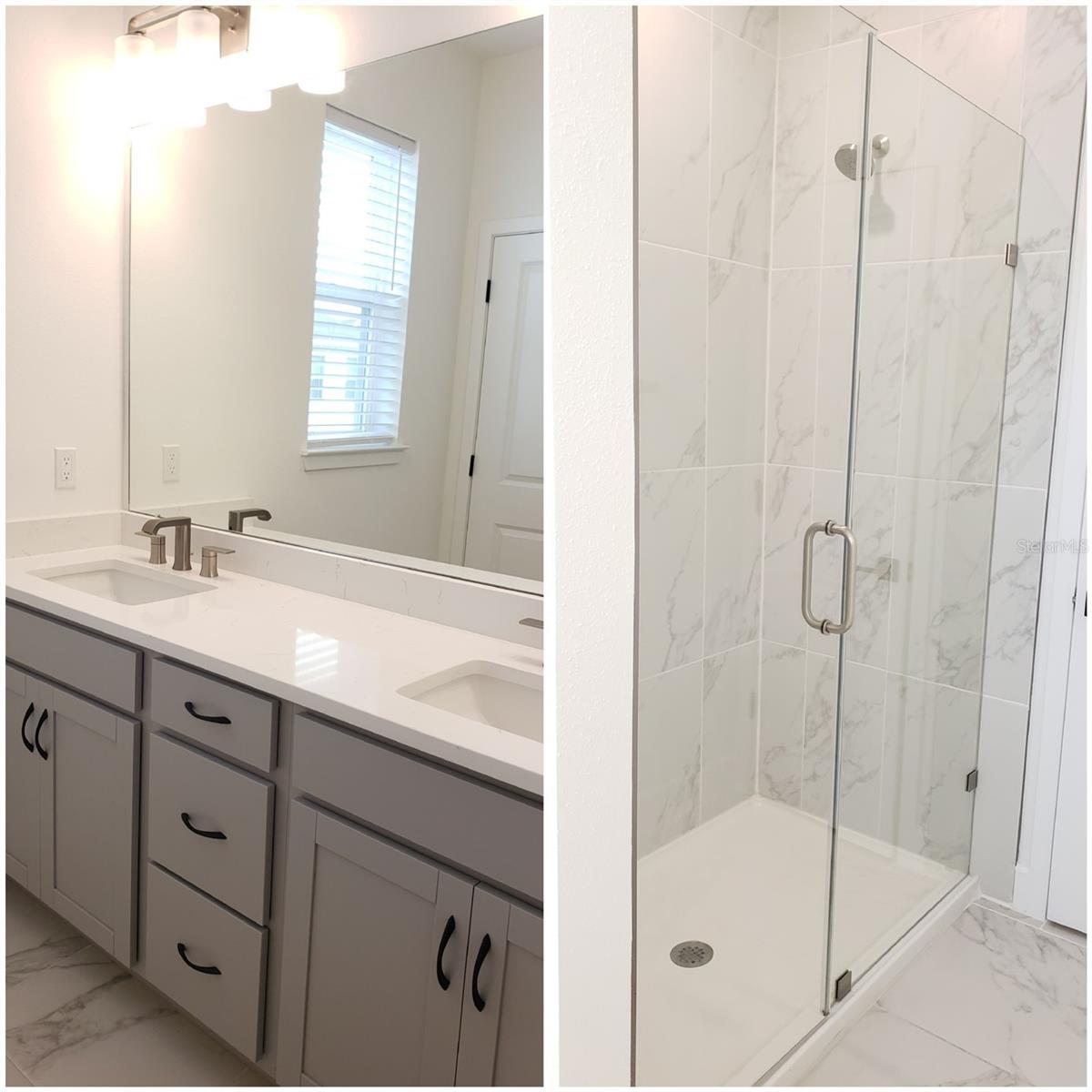Bathroom with a double-sink vanity and a glass-enclosed, marble-look tile shower.