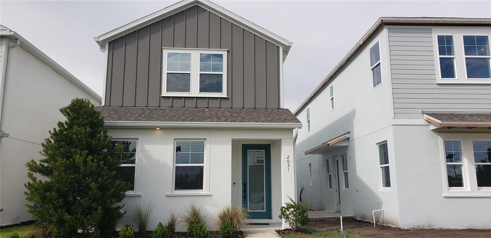 Two-story home with dark gray upper siding, white lower facade, and teal front door.