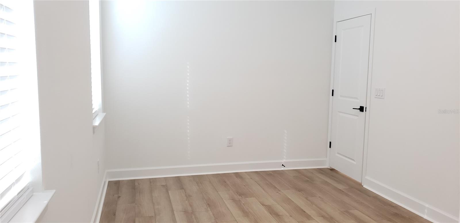 Empty bedroom with light wood-look flooring and windows fitted with blinds.