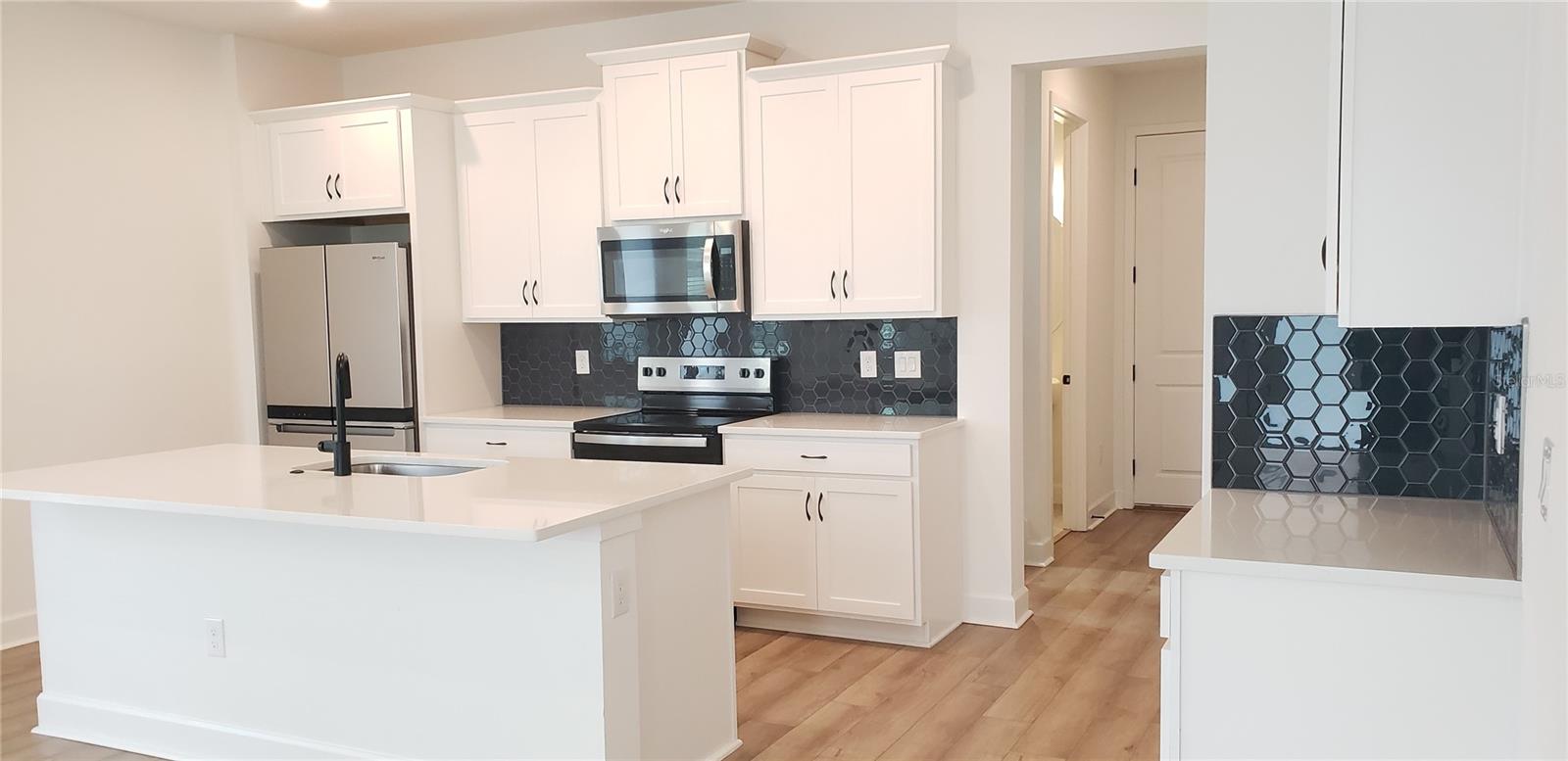 Kitchen with white cabinets, a large island, stainless steel appliances, and dark hexagonal backsplash.