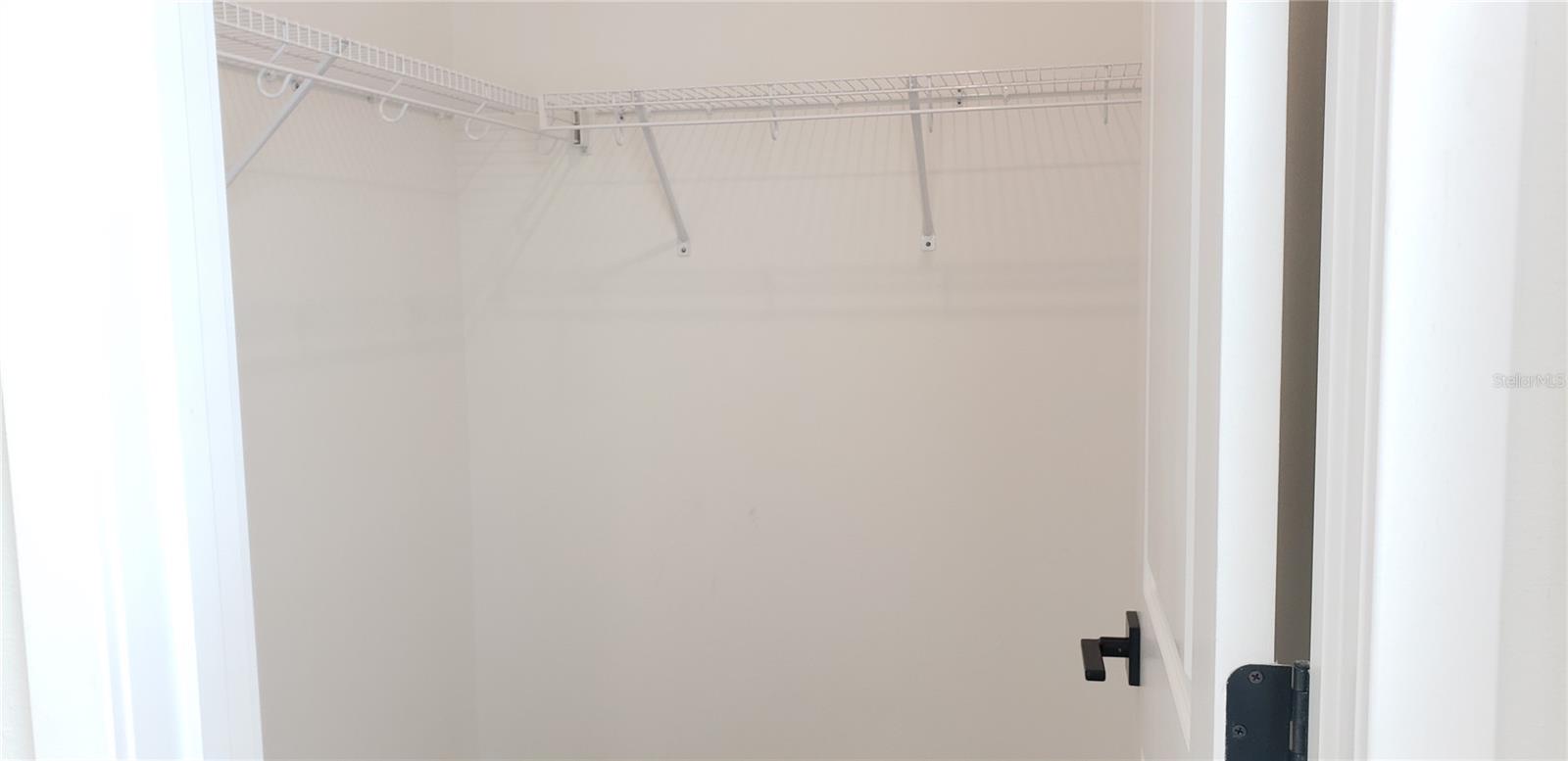 Empty walk-in closet with white wire shelving and hanging rods.