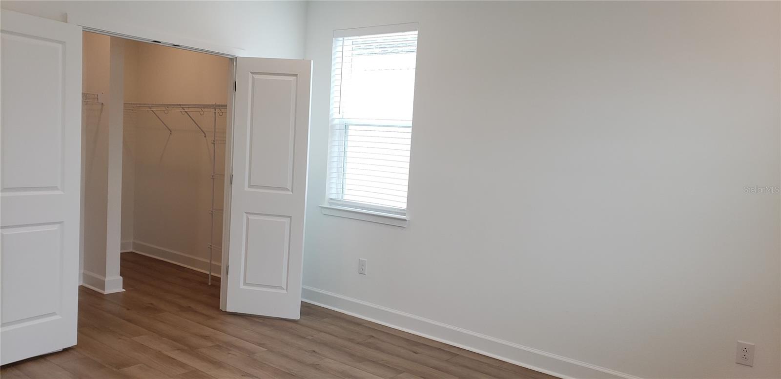 Empty bedroom with wood-look flooring, a window, and an open walk-in closet.