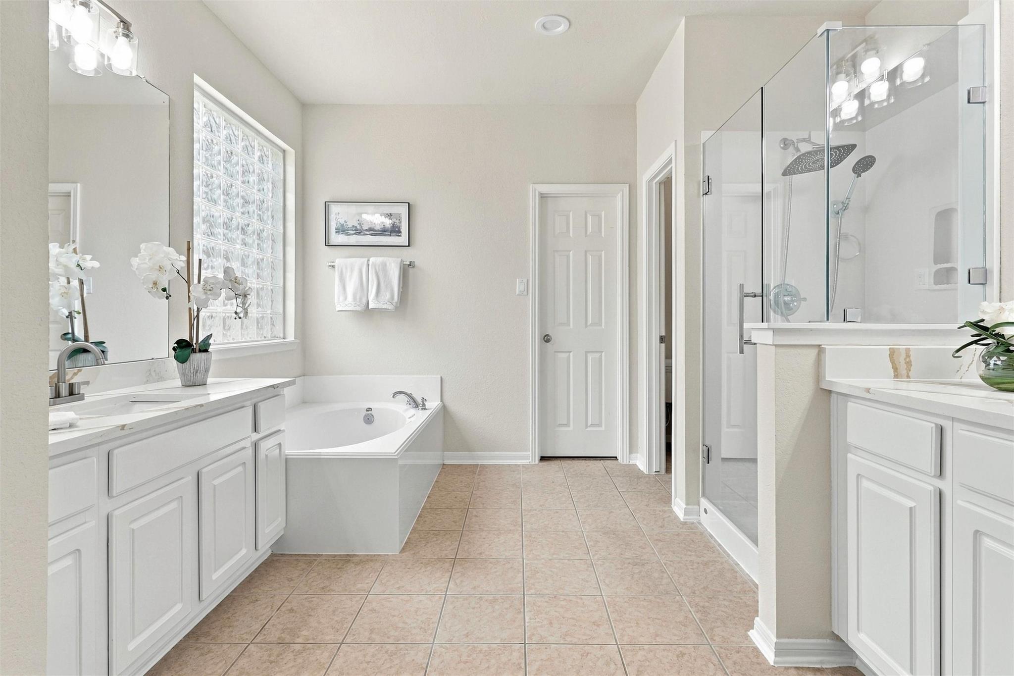Bright bathroom with glass-block window, corner soaking tub, and glass-enclosed shower.
