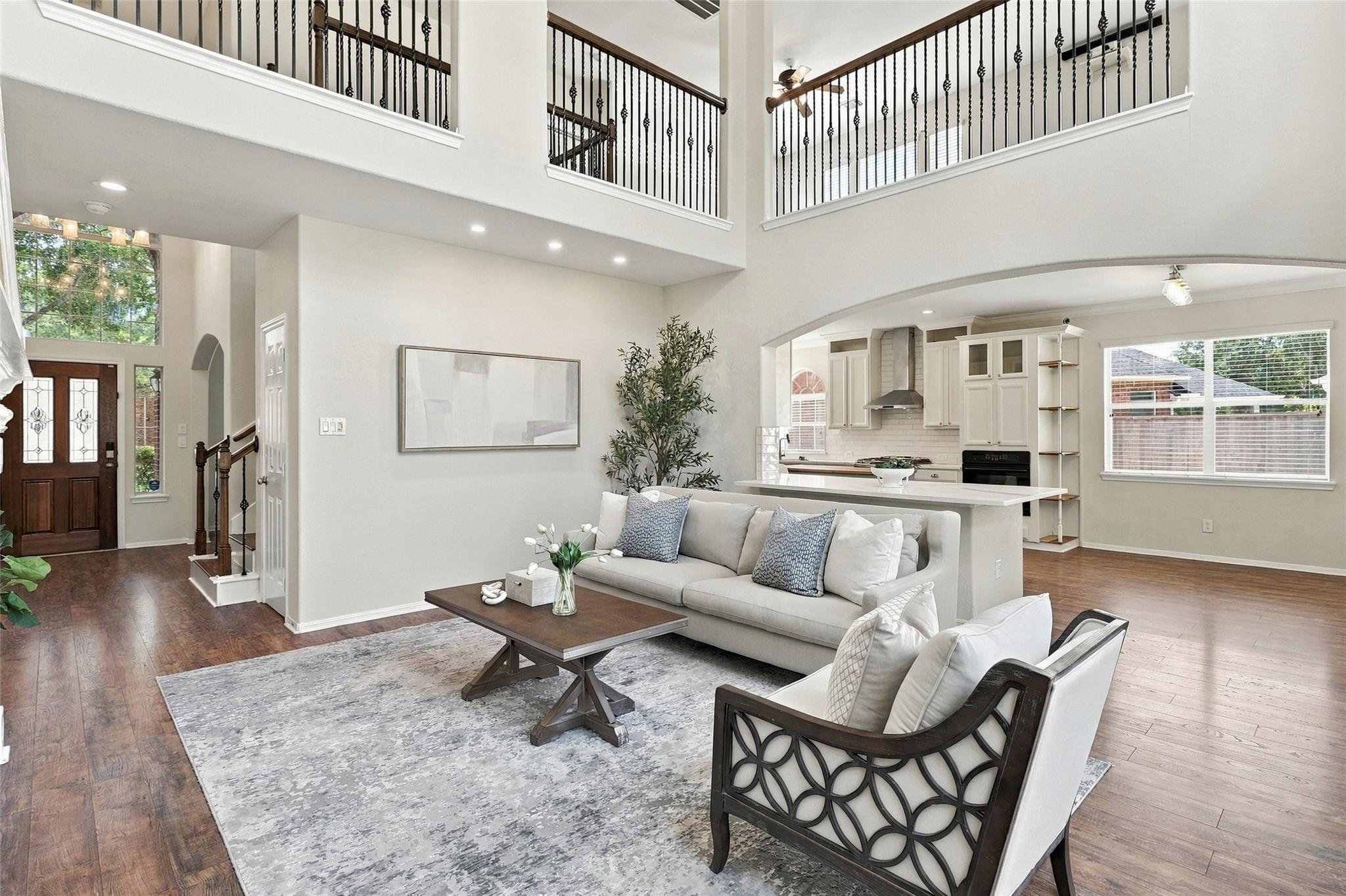 Open-plan living room and kitchen with double-height ceiling, upstairs balcony, and white cabinetry.
